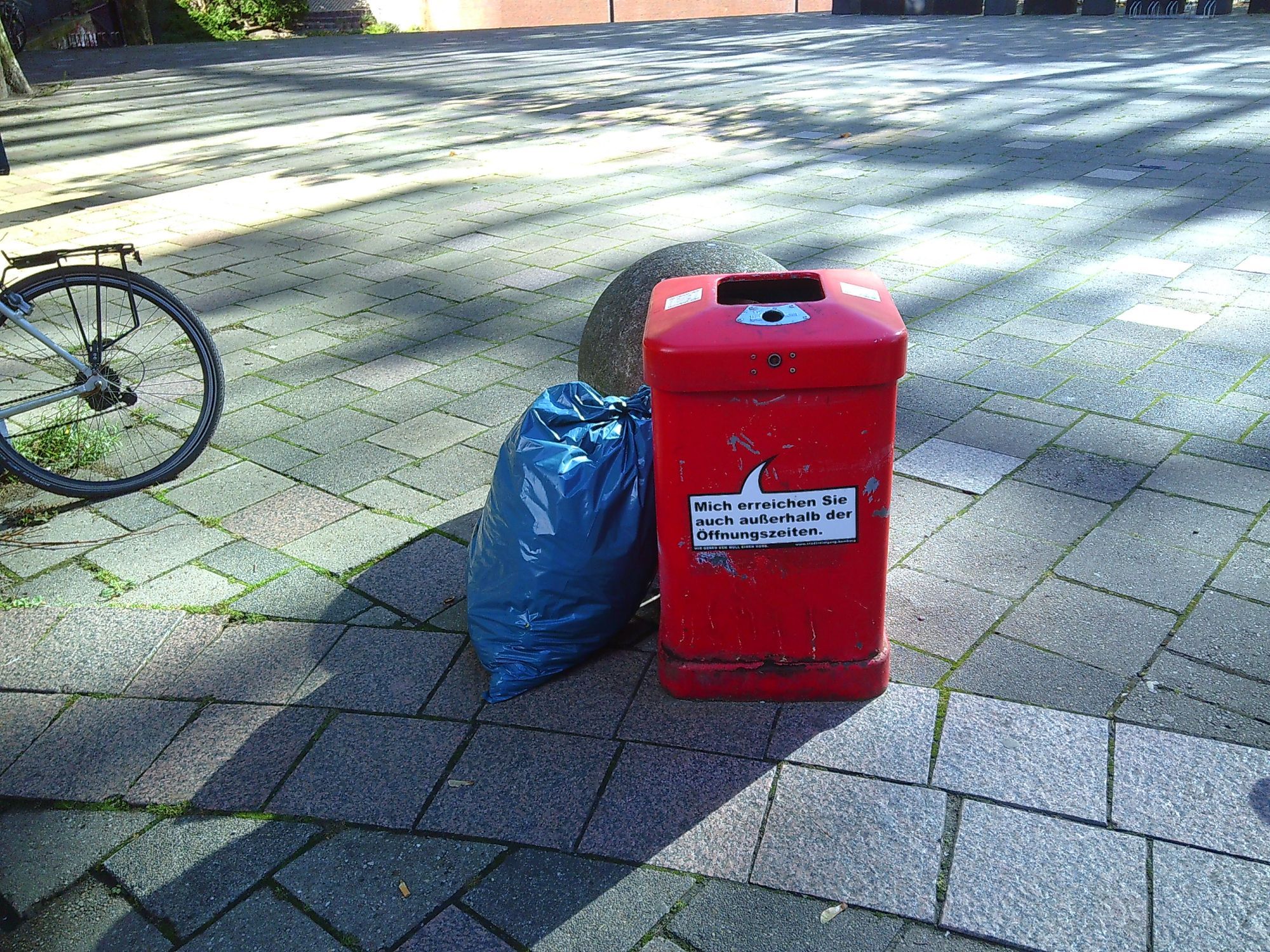 Rote Mülltonne, daneben steht ein Blauer Müllsack