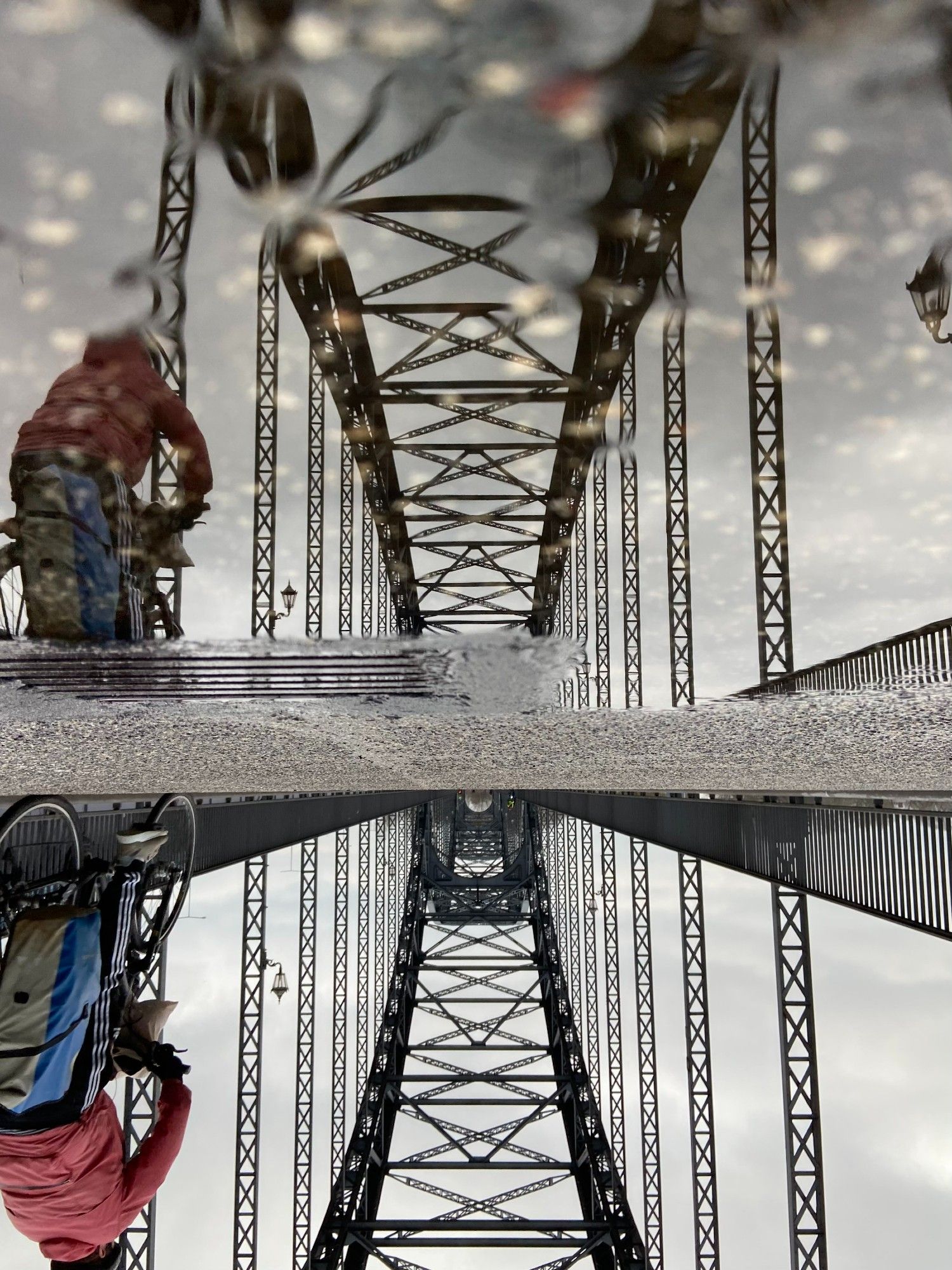 Brücke des 17.Juni in Harburg. Spiegelung der Brücke in einer Pfütze, auf der linken Seite fährt ein Fahrradfahrer durch