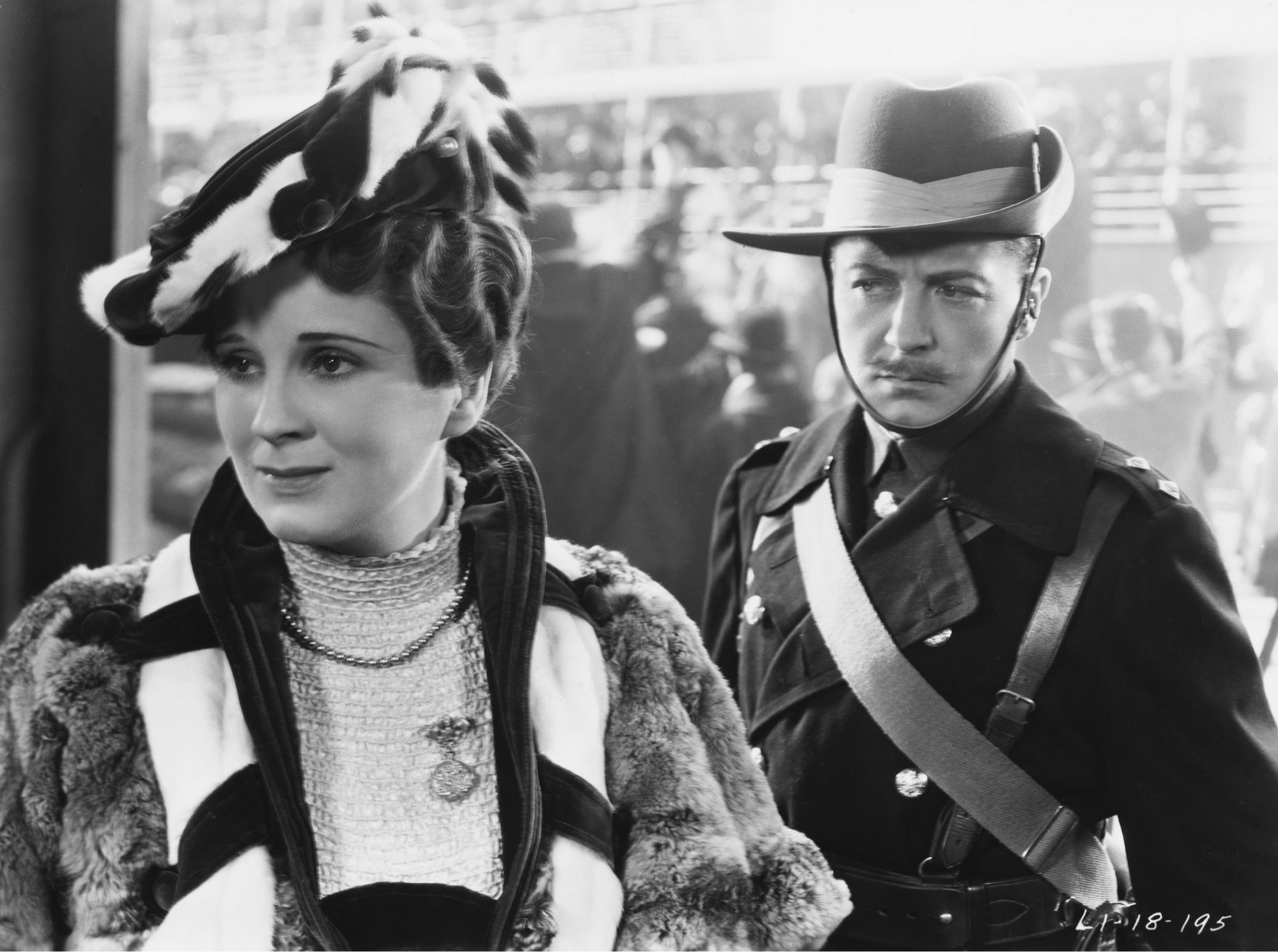 A man dressed as  a soldier foe the Boer War stands behind a woman who won’t look at him as he leaves to go to war