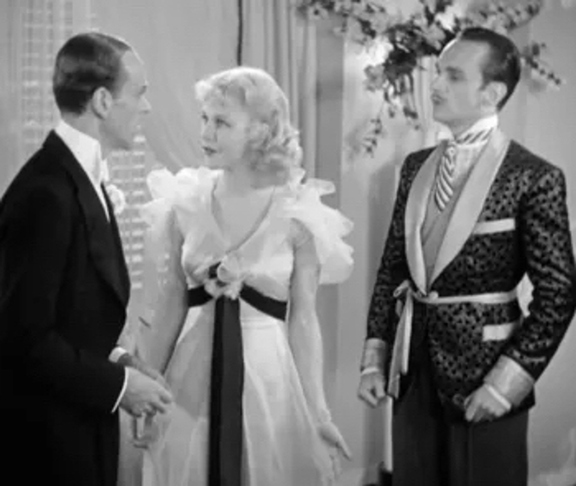 Guy (Astaire) looking at Mimi (Rogers) with Tonetti, the man paid to pretend to have an affair with her, standing behind