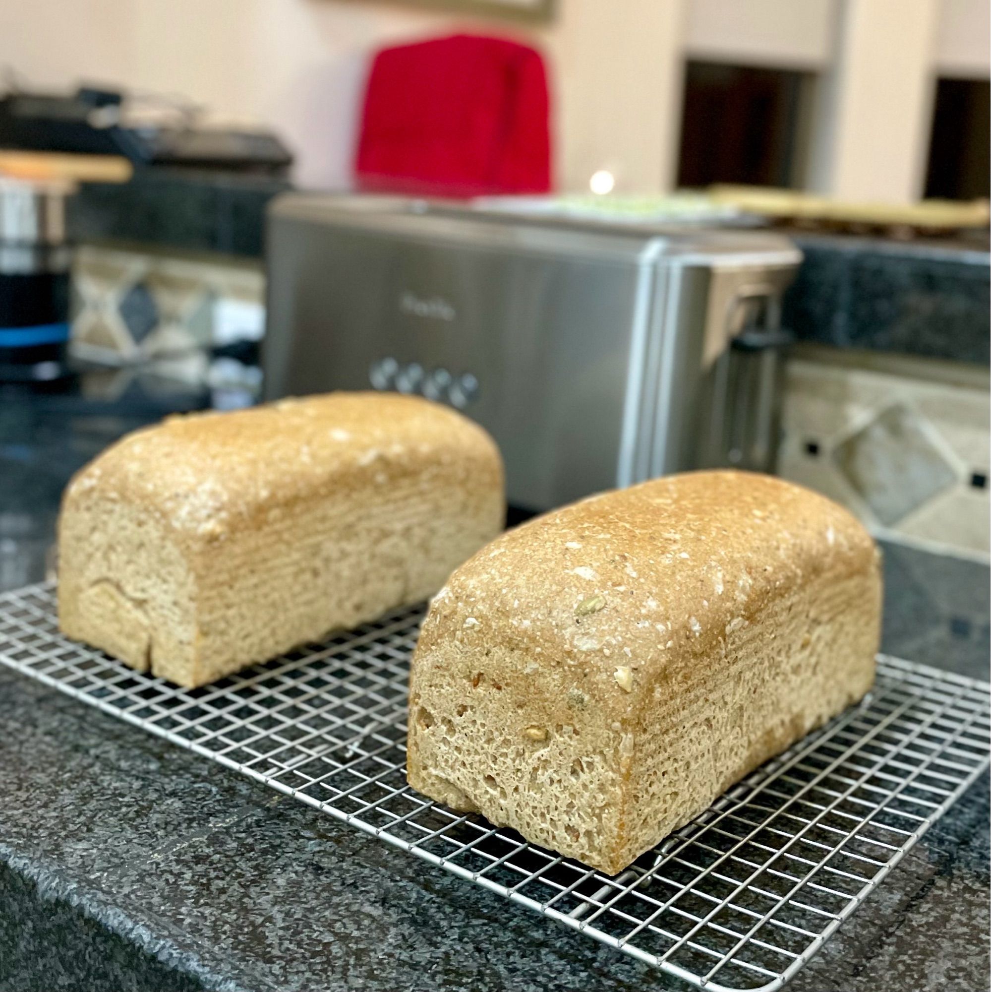 Two loaves of sandwich bread cool on a rack on a black granite countertop.