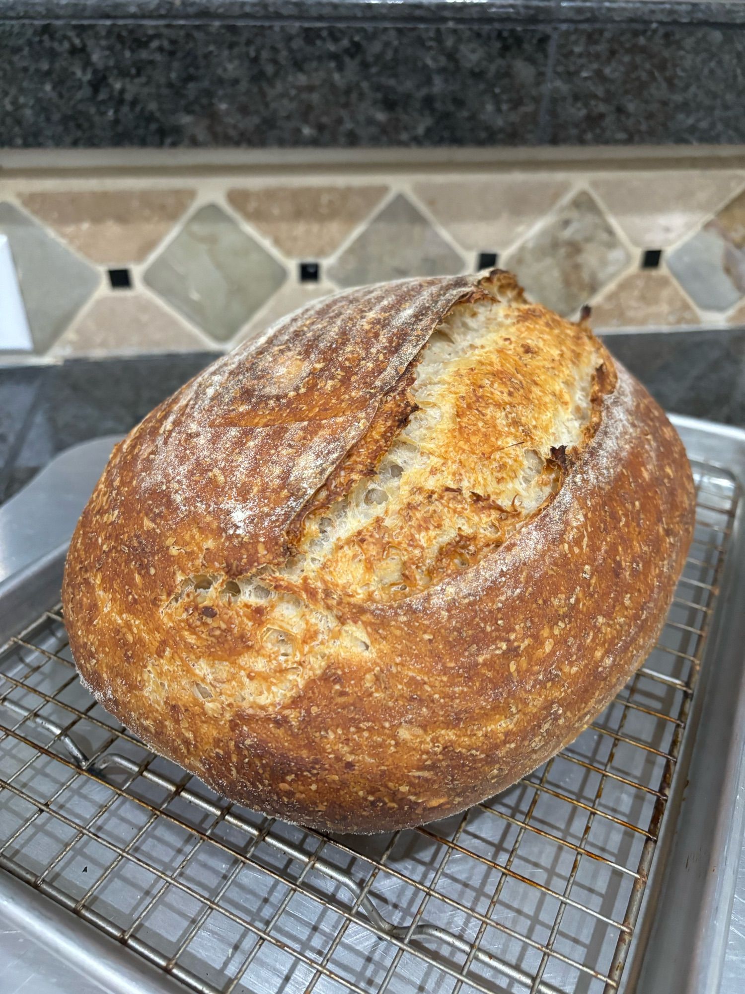 A freshly baked loaf of sourdough bread sits on a cooling rack