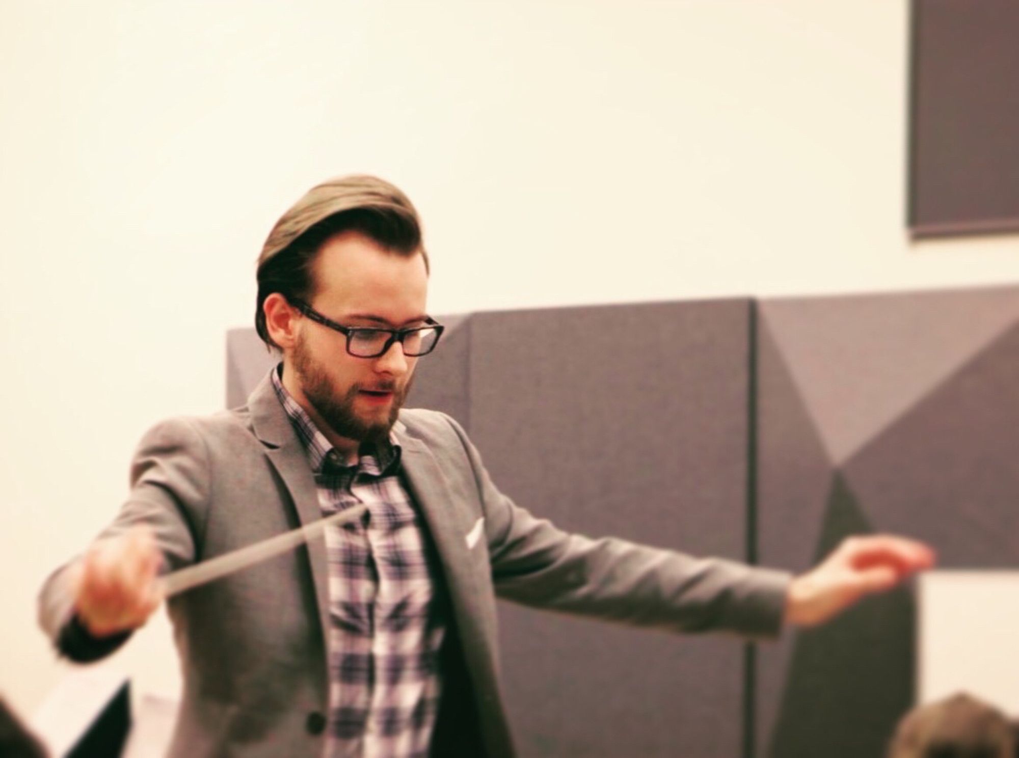 A man in a gray suit is conducting an orchestra.