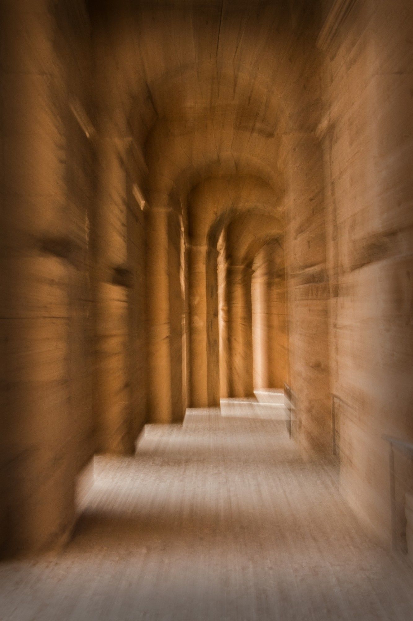 Series of high sandstone arches, retreating into the distance and curving away to the right. The picture has a blurred effect of motion towards a central point.