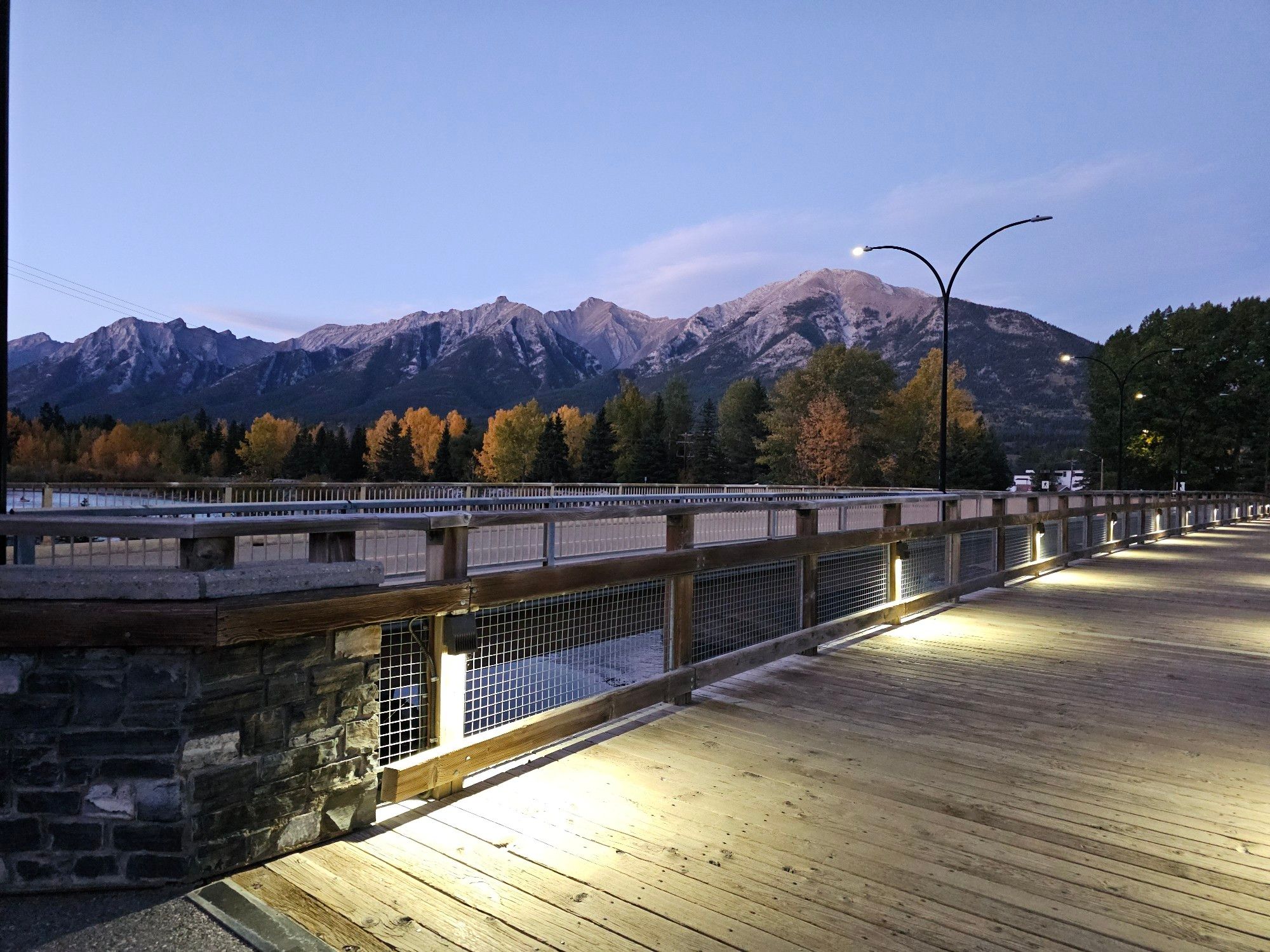 A lit up bridge with yellow and green trees and a mountain range in the background.