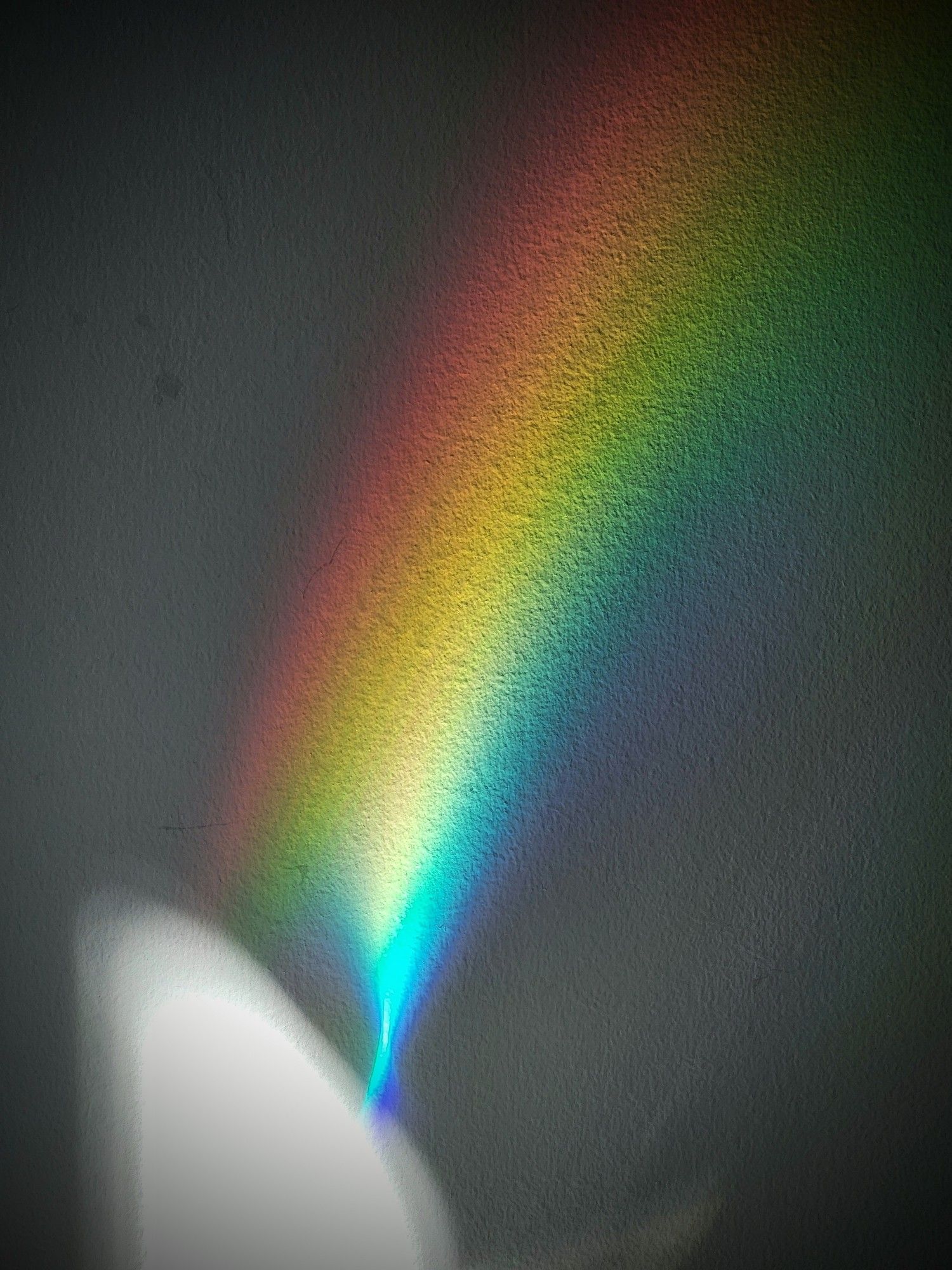 A spray of rainbow colours eminates up from an area of the wall lit up by a sunbeam. Most of the rest of the wall is dark, untouched by the rays bouncing of the CD or coming from the Sun.