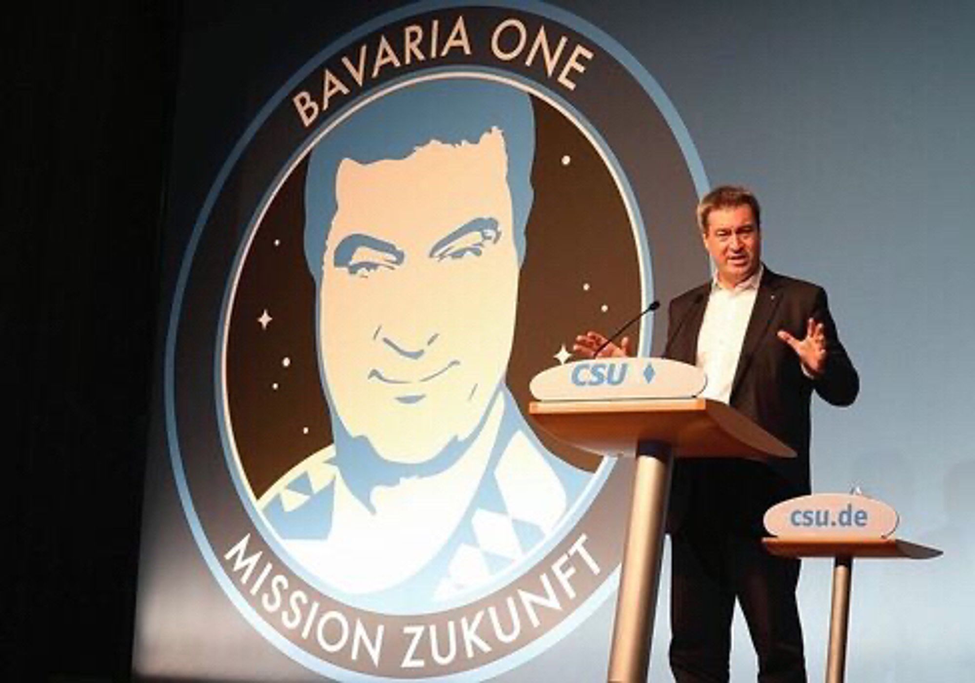 Söder am CSU Rednerpult, im Hintergrund das Logo von Bavaria One, Mission Zukunft, welches überdimensioniert das Gesicht von Söder zeigt.