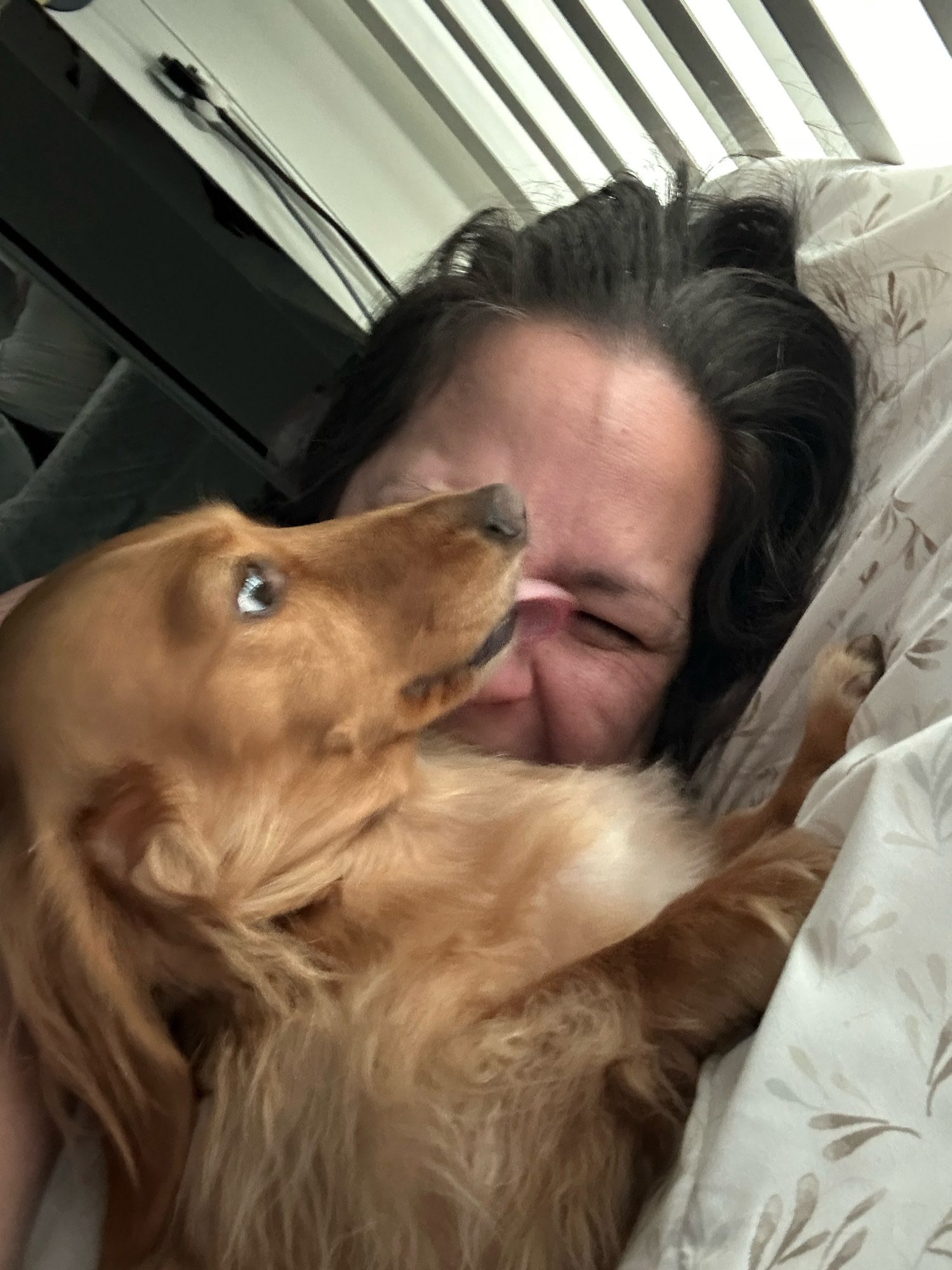 Photo of Jack laying in front of my face trying to give sideways kisses on my face. He is smushing up against my face and I’m making a laughing-squinting face.