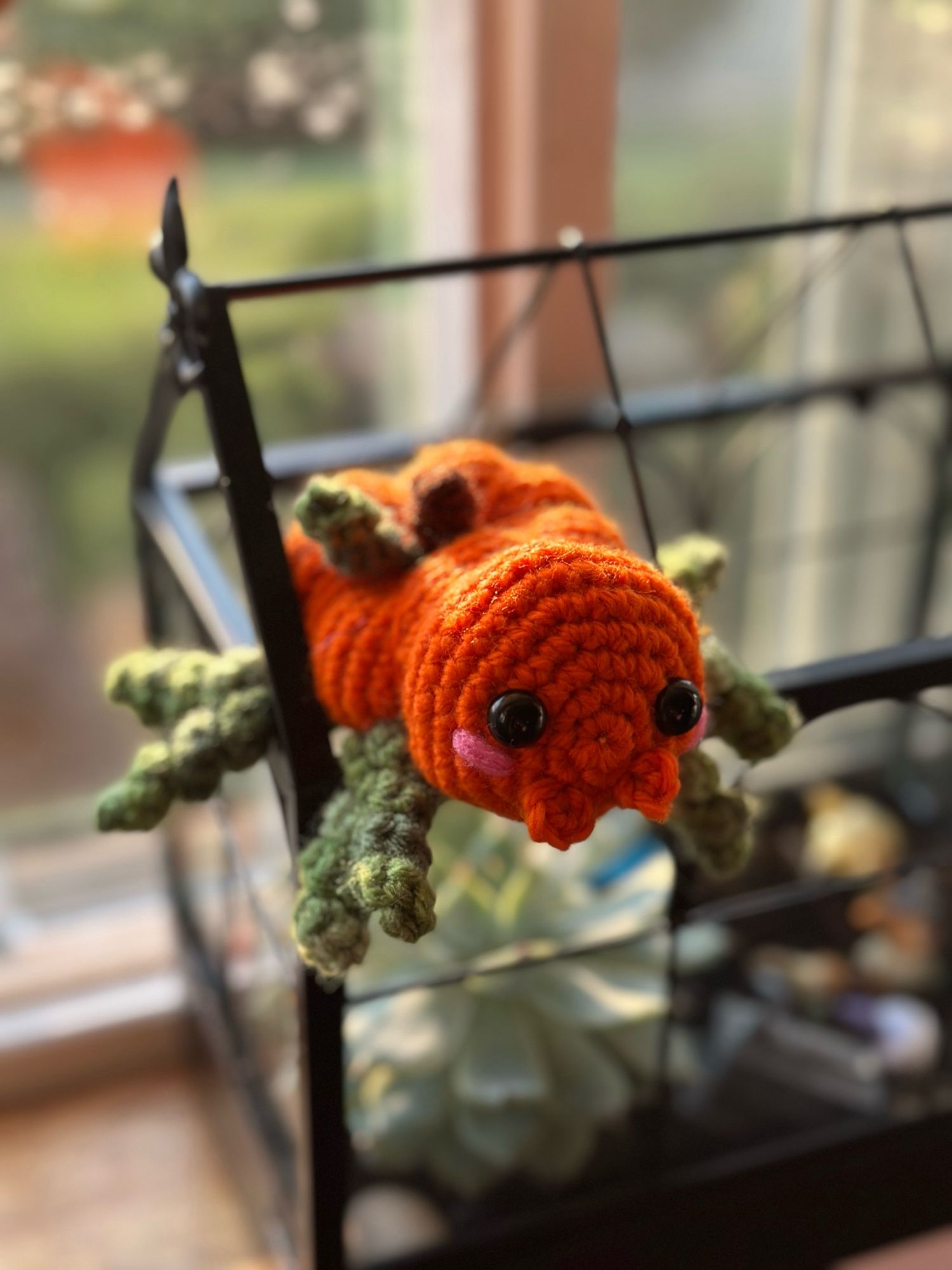 A photo of a crocheted spider made to look like a pumpkin. The body is orange, the legs are green, and it has a little stem and vine on its back