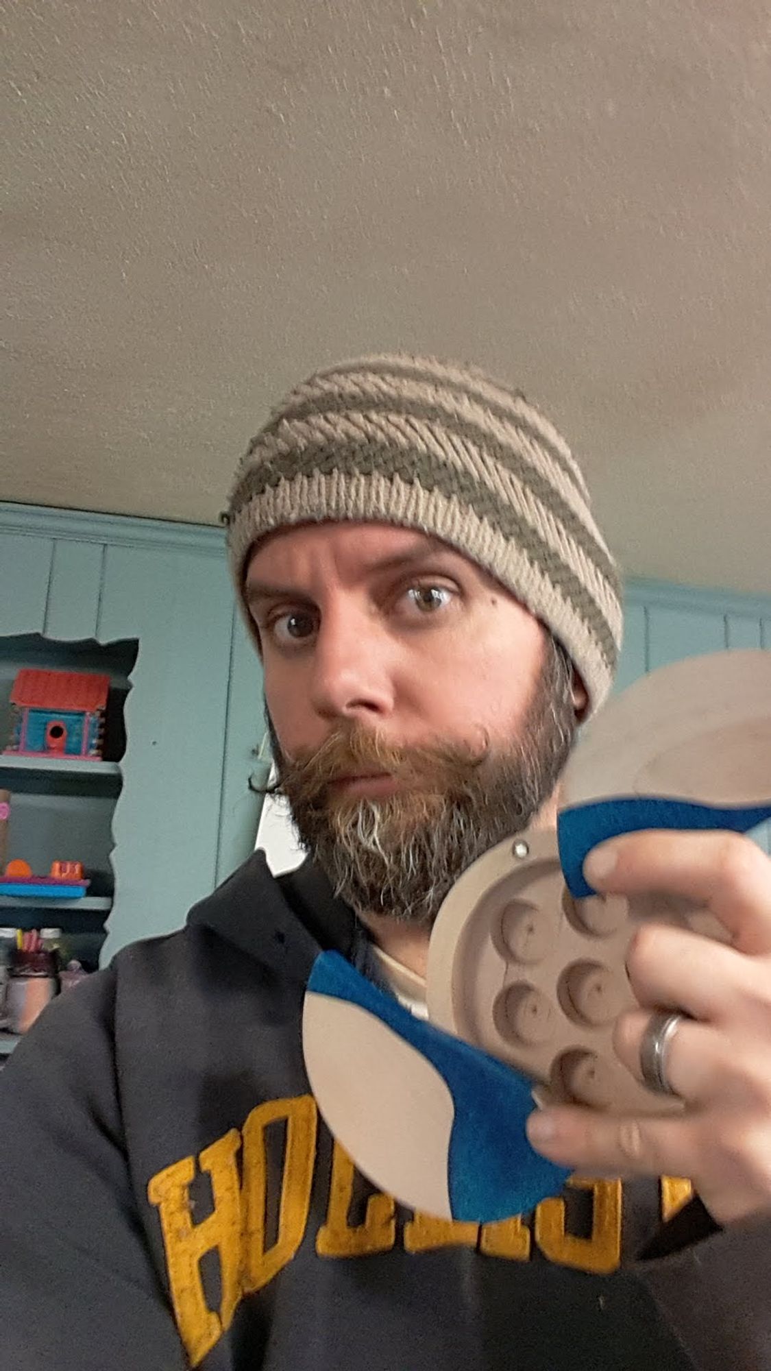 Pic of me holding a dice box wearing a hat and sweatshirt with a curled mustache and beard.