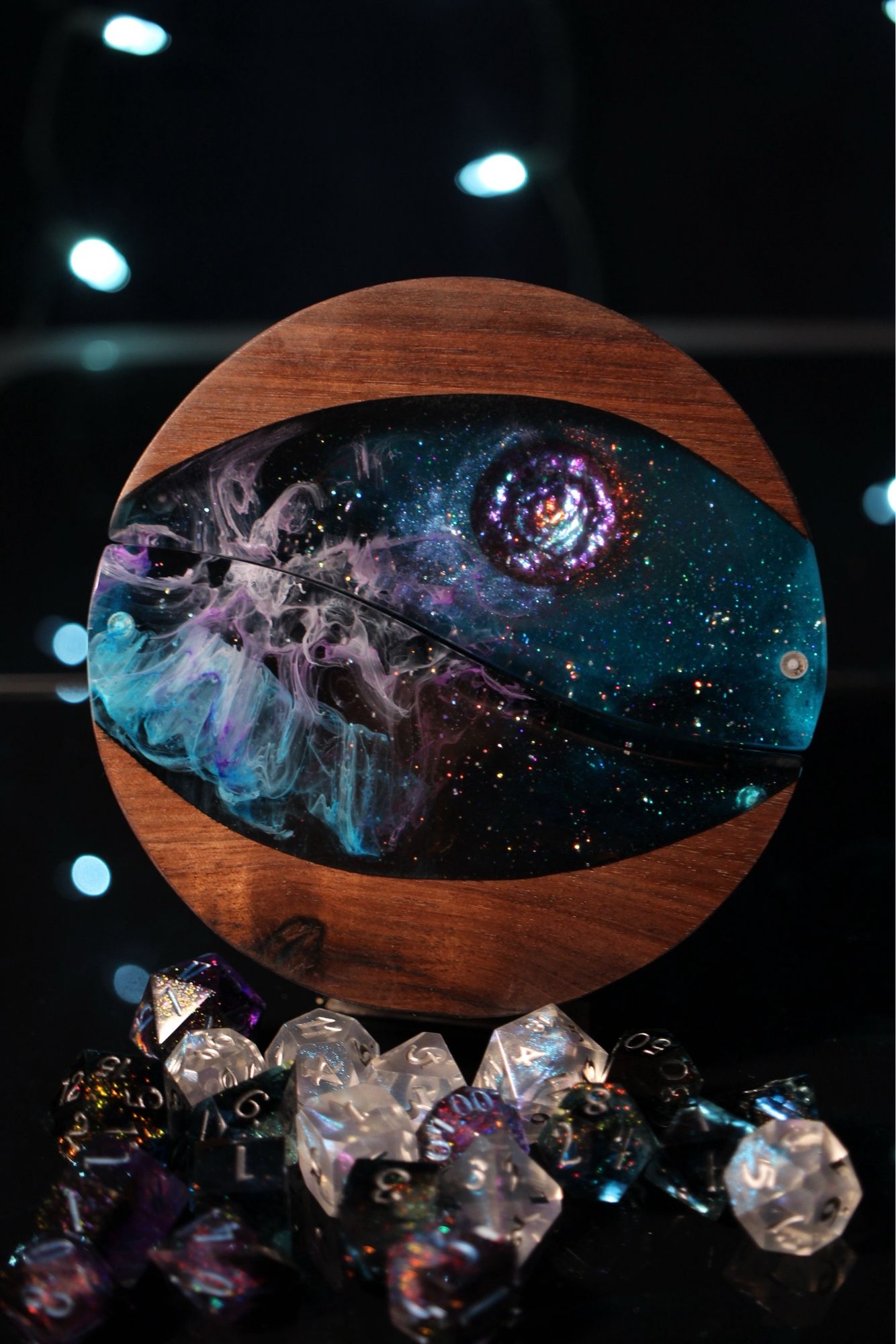 Round walnut dice box with a large oval cutout filled with space looking epoxy and a purple iridescent comet and purple and blue vapor trailing behind