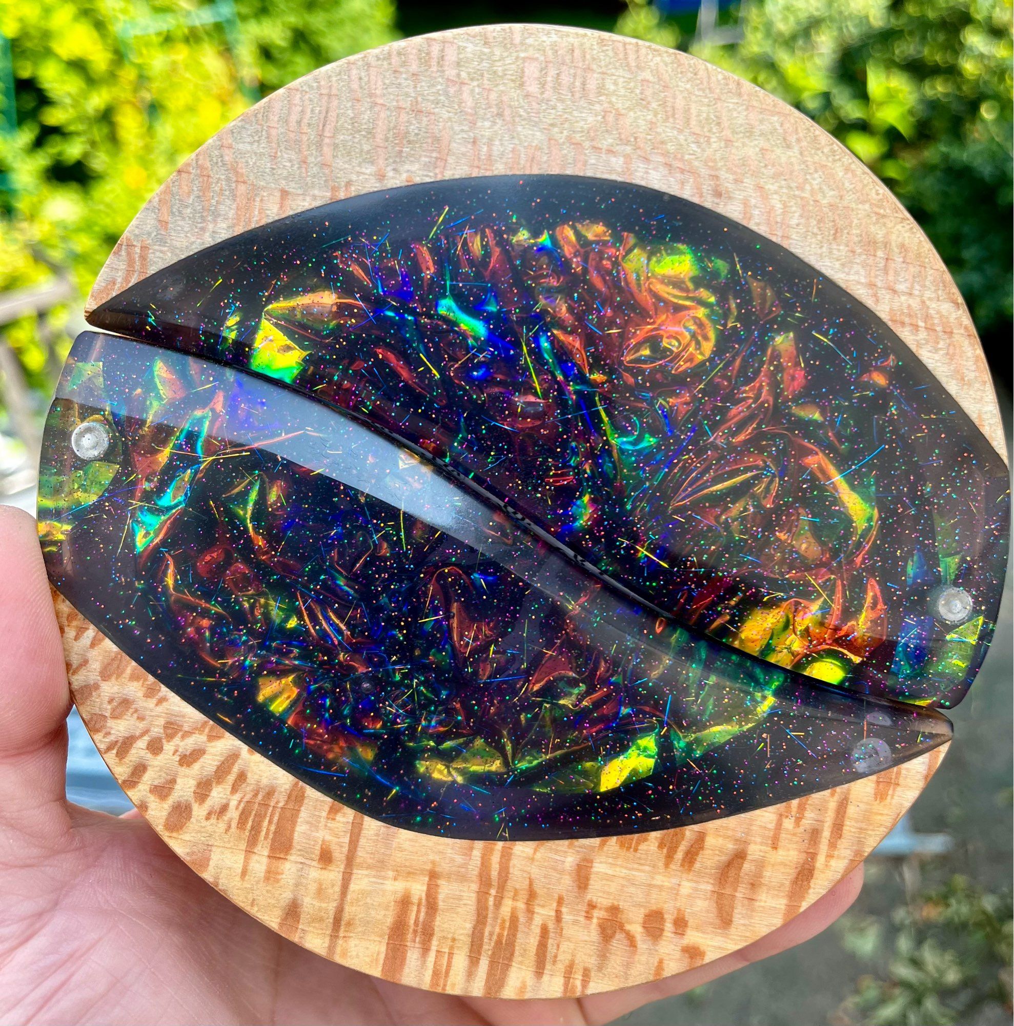 Round Sycamore dice box with a large oval cut out, filled with iridescent foil of yellow, green, orange and blue as well as dark epoxy.