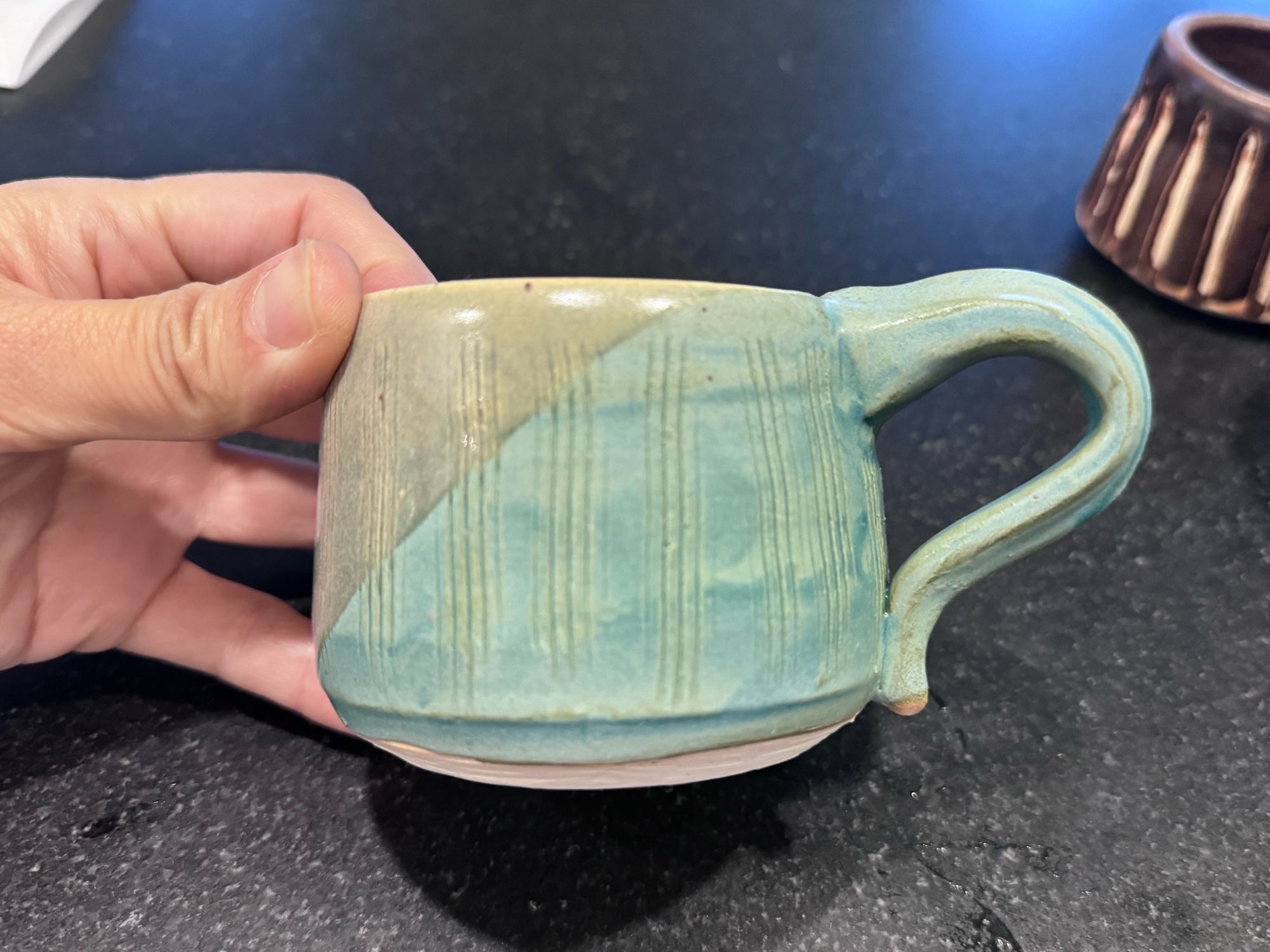 A handmade mug, glazed with flat pale green on the handle side and oatmeal on the left side, in a diagonal dip.