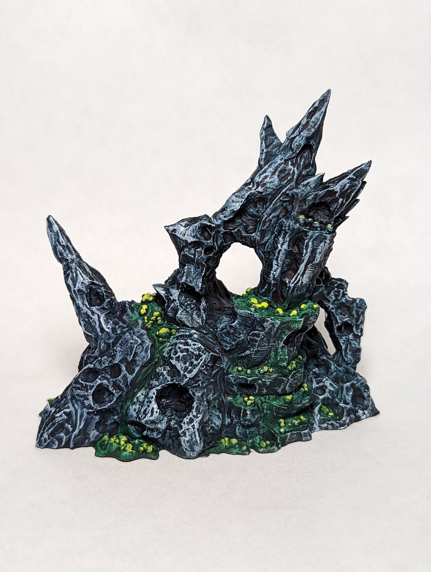 Miniature model of Black sharp pointed rocks covered in green sludge, and yellow bubbles.