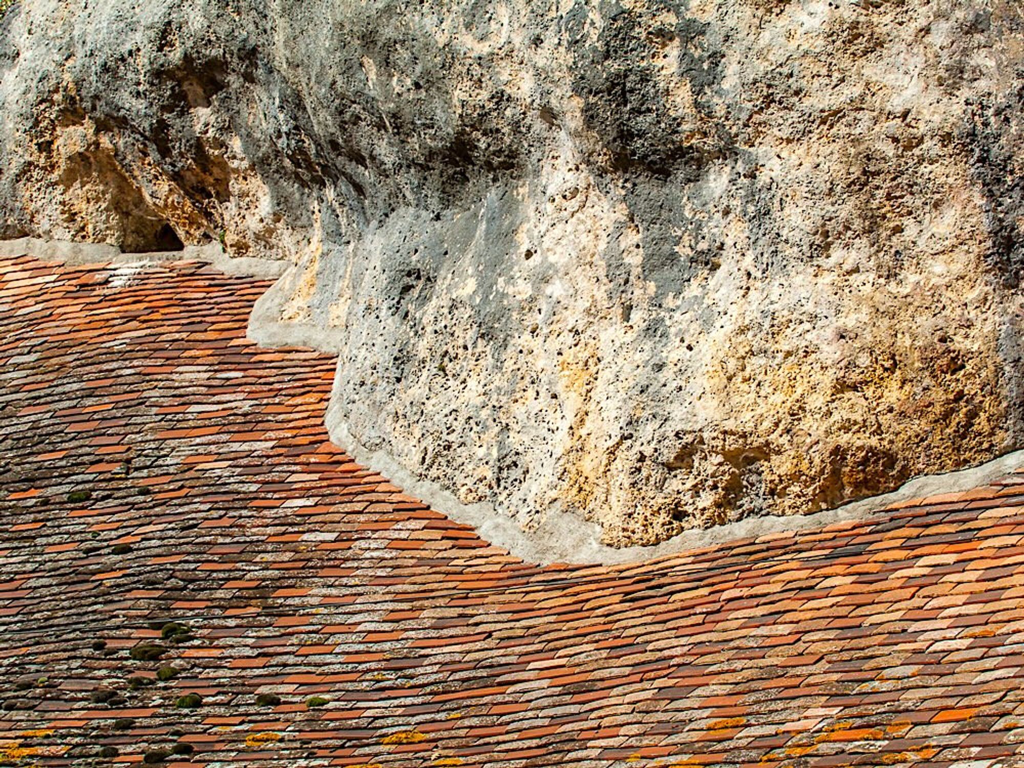 Traditional terracotta tiles with an undulating roof-line where the domestic building's roof joins the uneven limestone rock face.