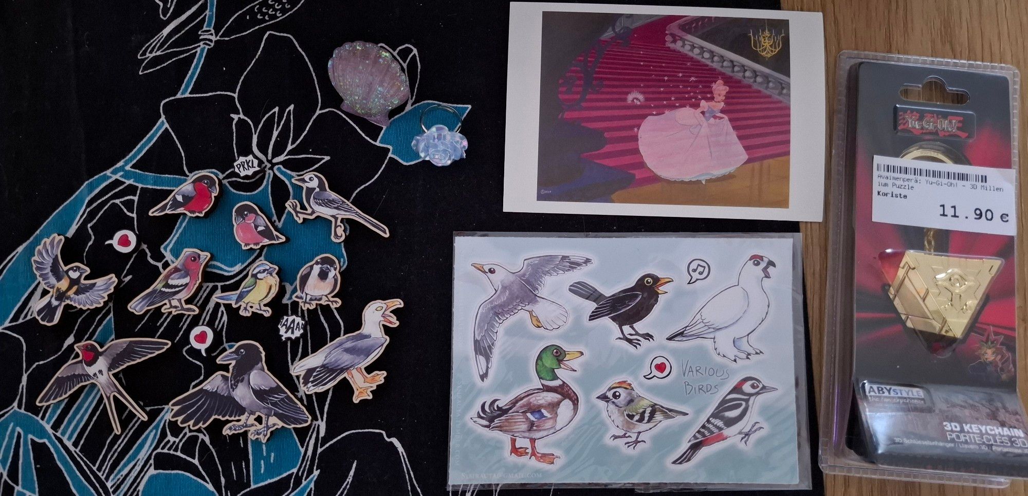 on the left: a collection of fridge magnets featuring different birds and speech bubbles, also two pretty rings
on the center: Cinderella postcard and sticker sheet featuring birds
on the right: Millennium puzzle keychain