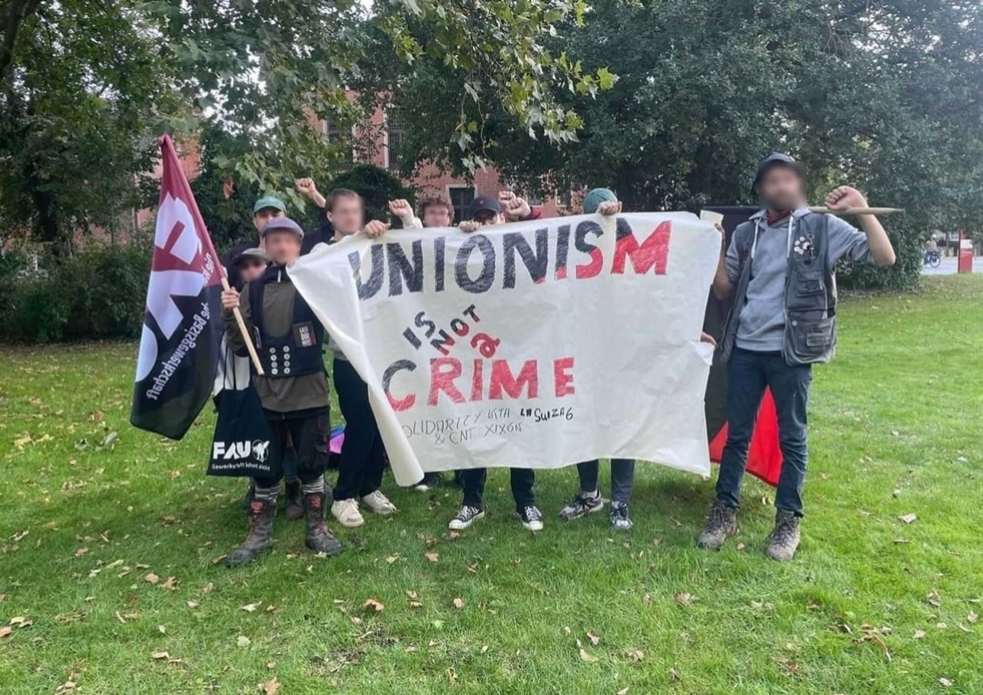 Mehrere Menschen, die die Faust heben. Einer trägt eine FAU Fahne. Gemeinsam halten sie ein Banner auf dem "Unionism is not crime" steht