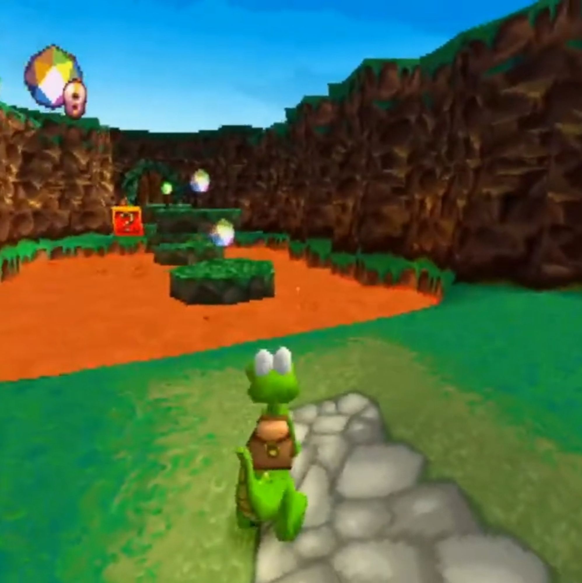 Croc: Legend of the Gobbos screenshot. Croc in a grassy field with some lava in the distance.