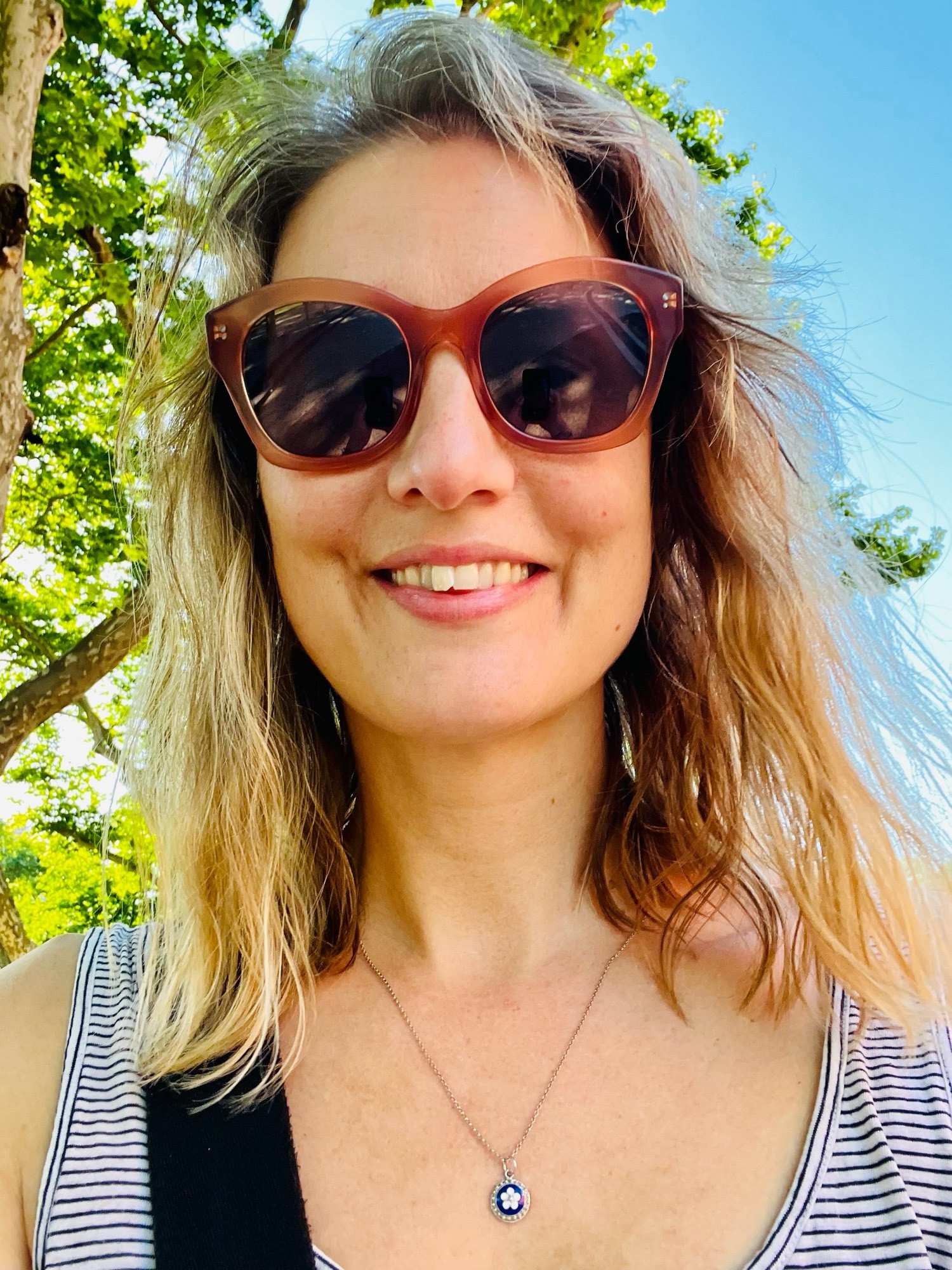 Selfie of Molly with green eucalyptus tree leaves and blue sky behind her.