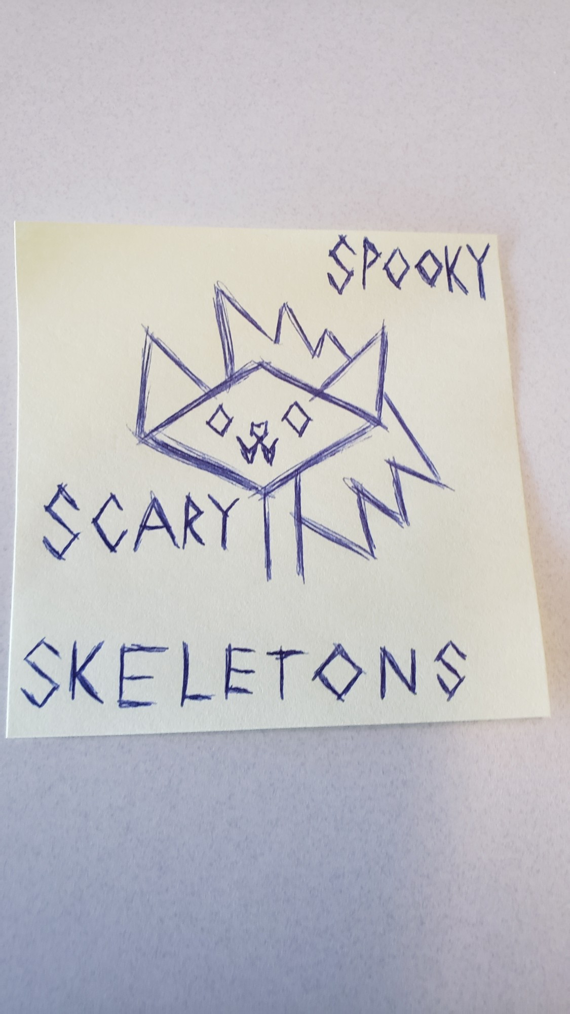 A doodle on a sticky note of a stylized cat skull with a mullet. "Spookt Scary Skeletons" is written around it