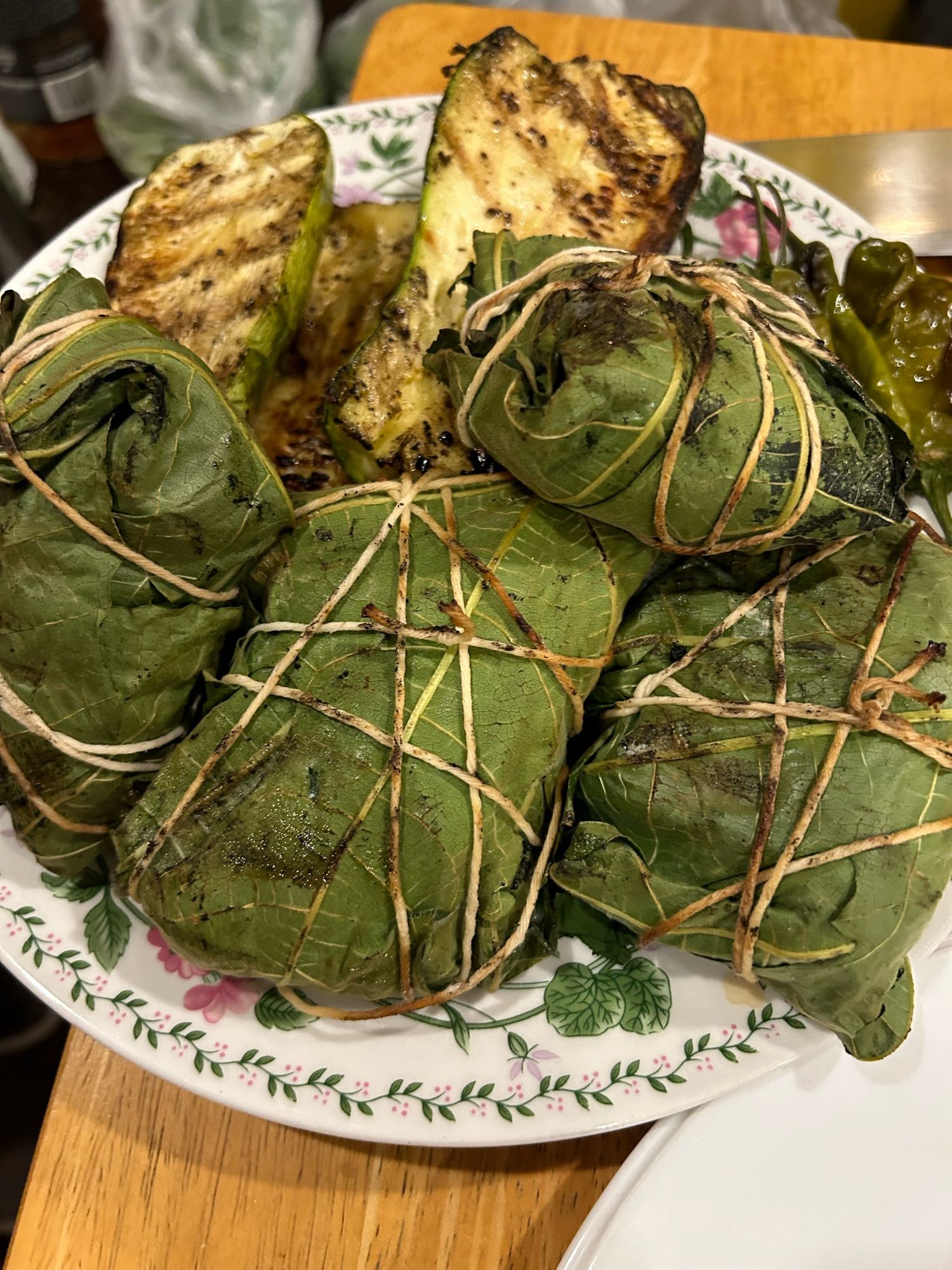 Fish wrapped in fig leaves tied with twine and grilled zucchini on a flowered plate.