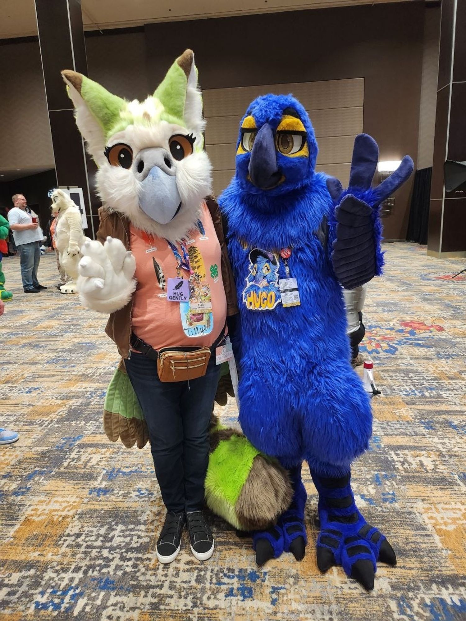 2 bird fursuits posing for a picture. A Kakapo gryphon and a hyacinth macaw.