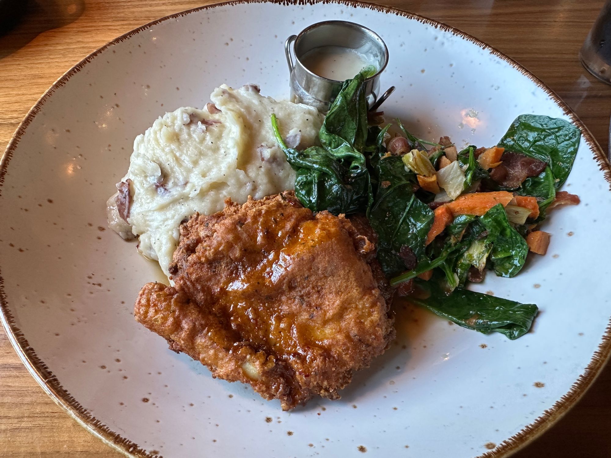 A plate of food: hand-dipped buttermilk boneless chicken breast, red skin potato mash, white gravy, spiced maple syrup, sautéed spinach with smoked bacon