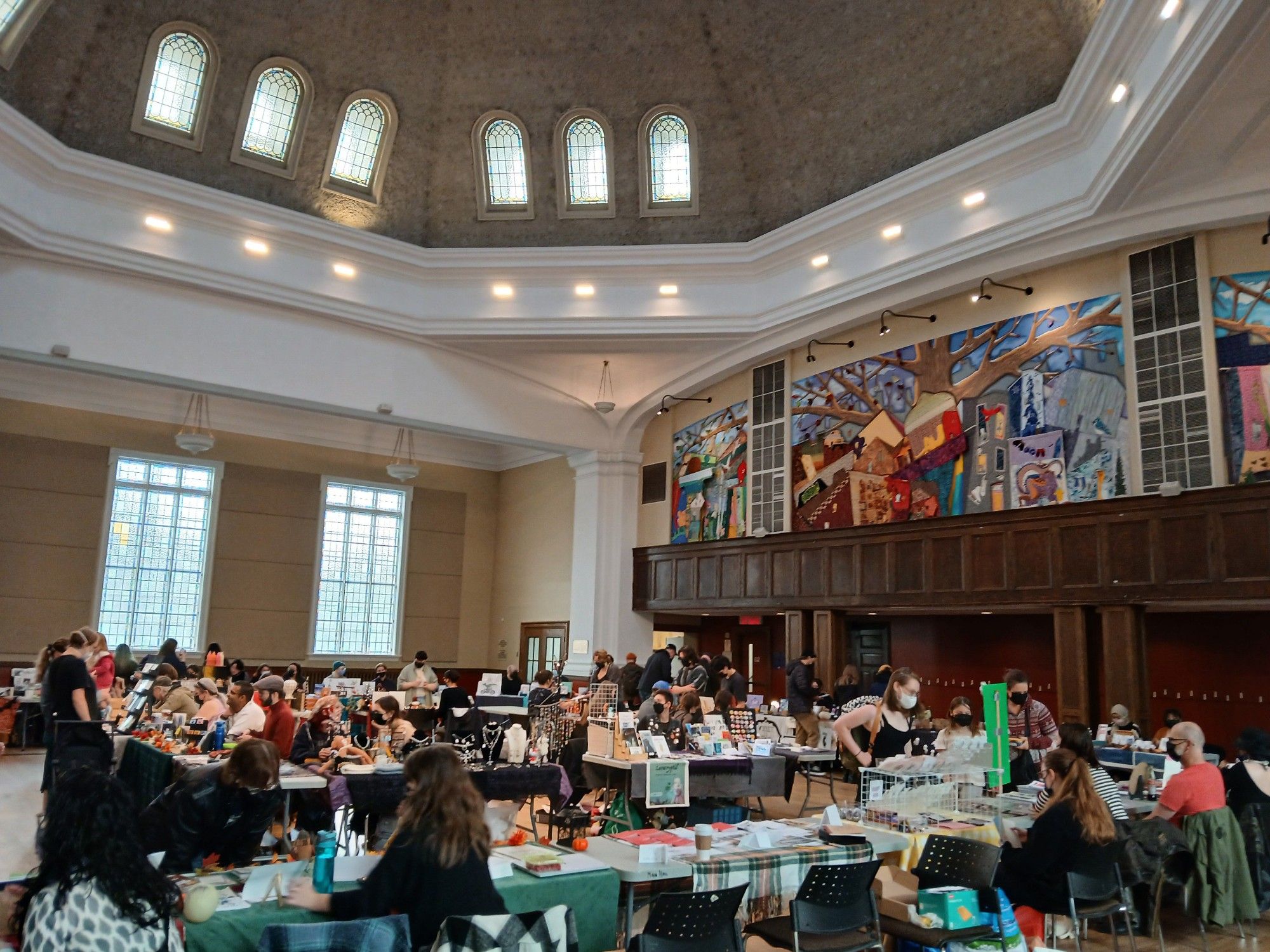 Domed community centre main hall with mural on high wall and tables full of artists