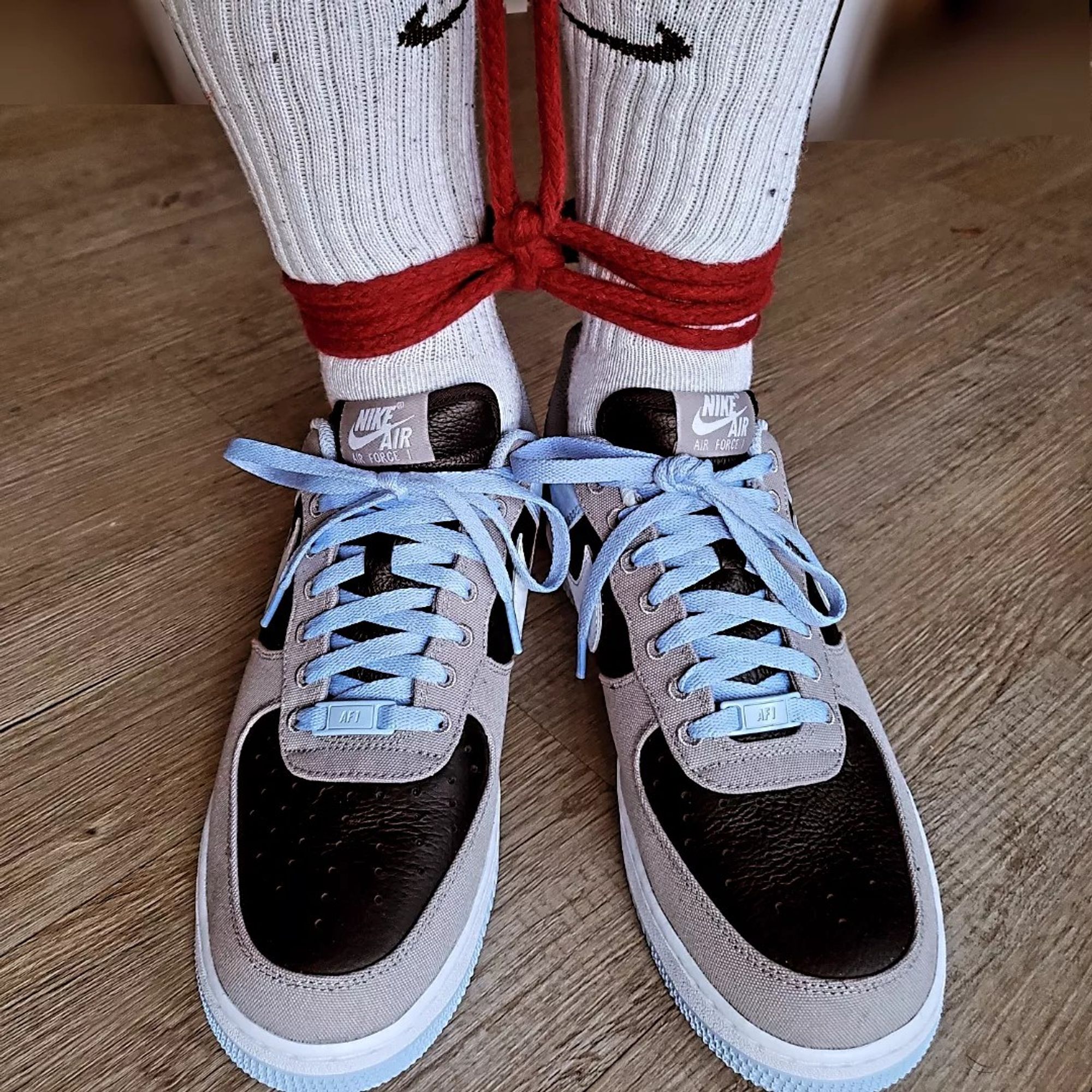 Ankles tied together by red rope;  wearing light blue, black and grey Nike AF1 and white socks