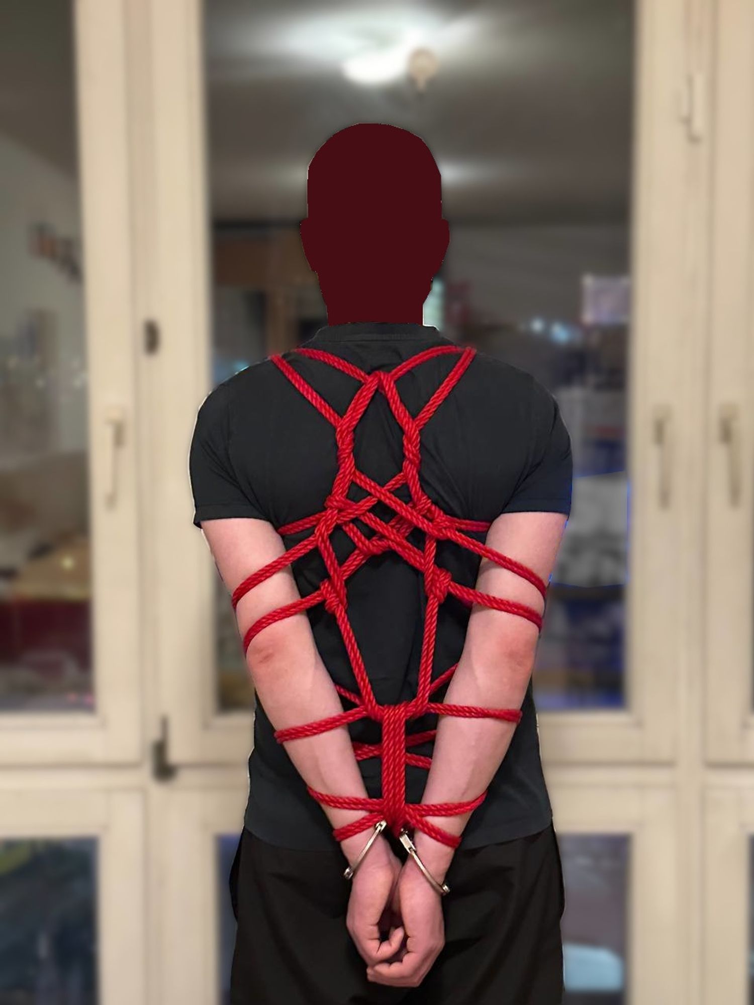 Man with arms behind his back in rope bondage and also handcuffed.