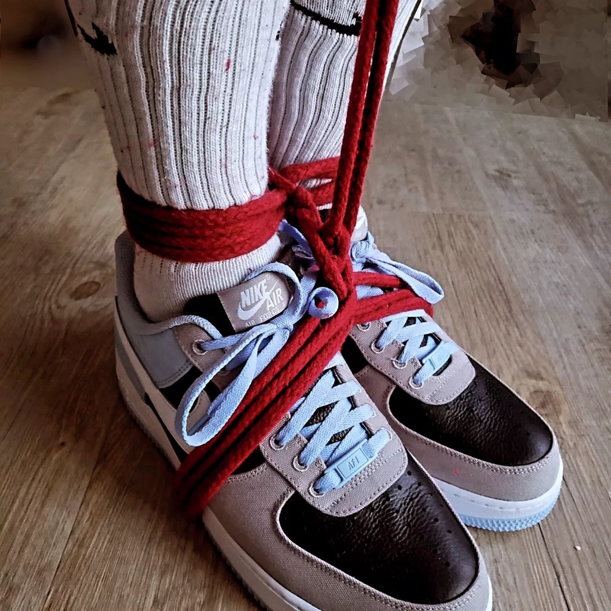 Ankles and shoes tied together by red rope;  wearing light blue, black and grey Nike AF1 and white socks