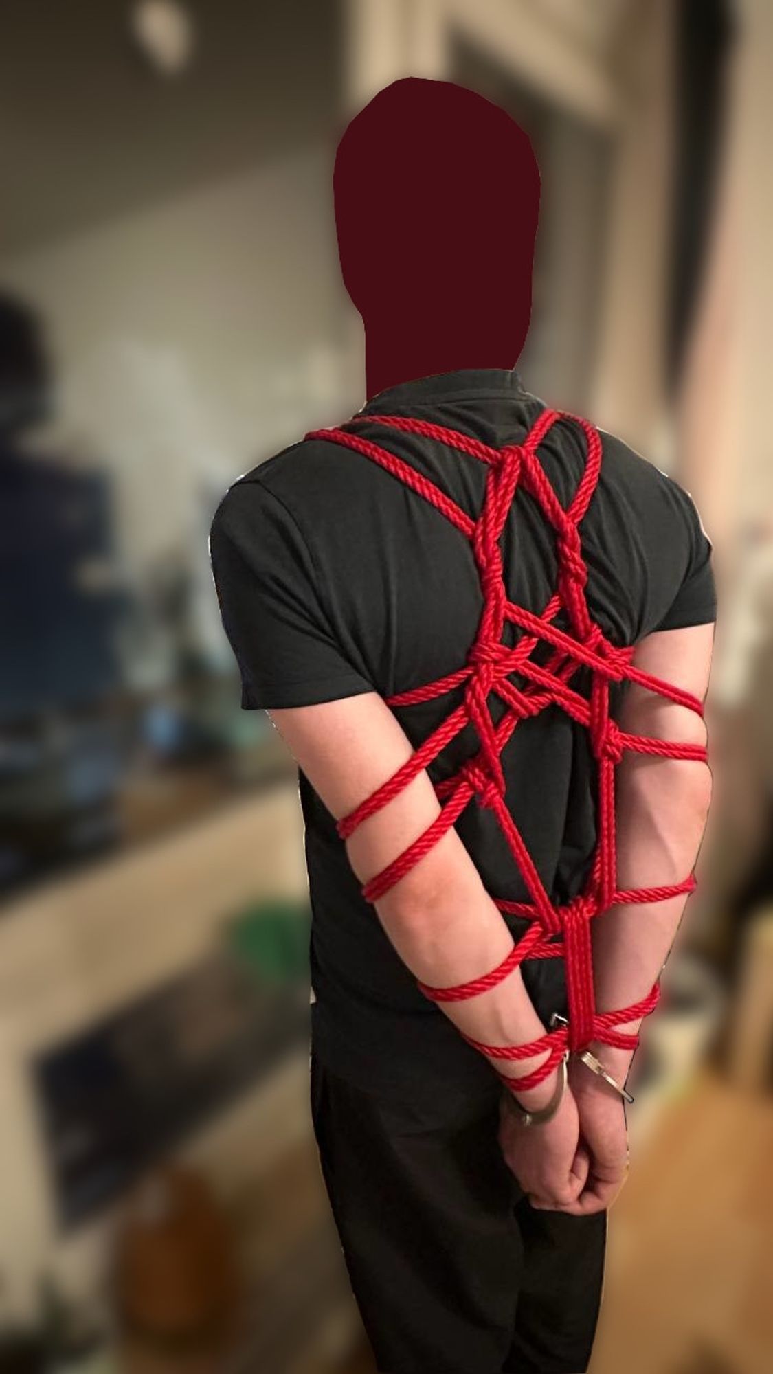 Man with arms behind his back in rope bondage and also handcuffed.