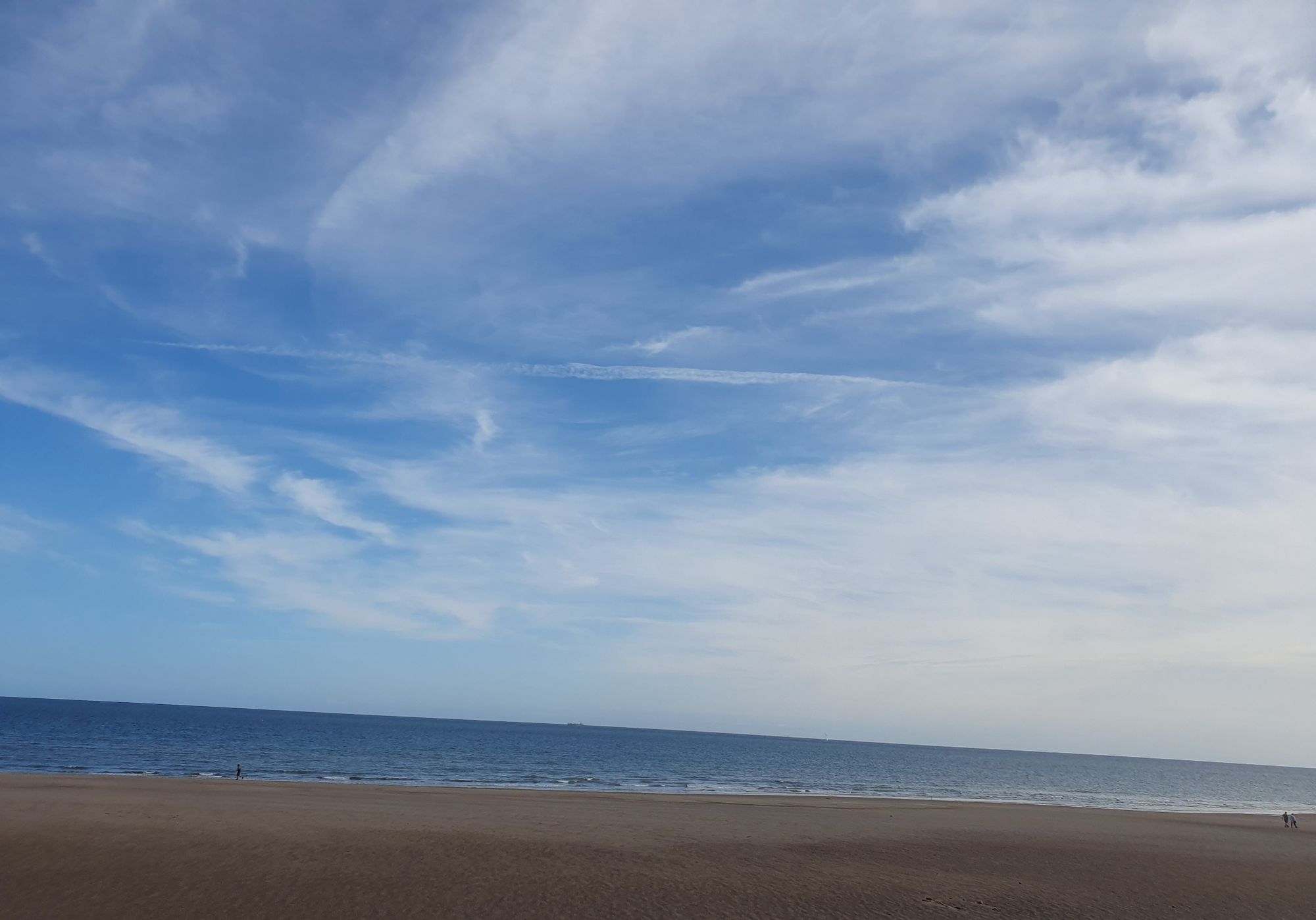 Photo shows a yellow sandy beach leading down to the sea, with a big blue sky above