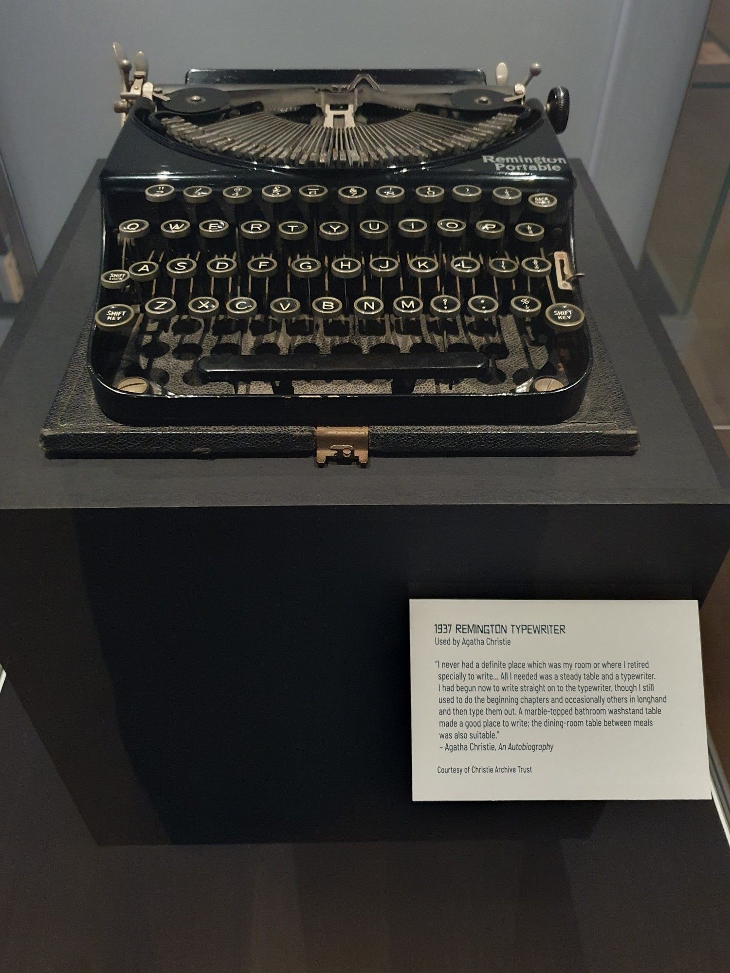 Photo shows an old, rather shabby black typewriter in a display case