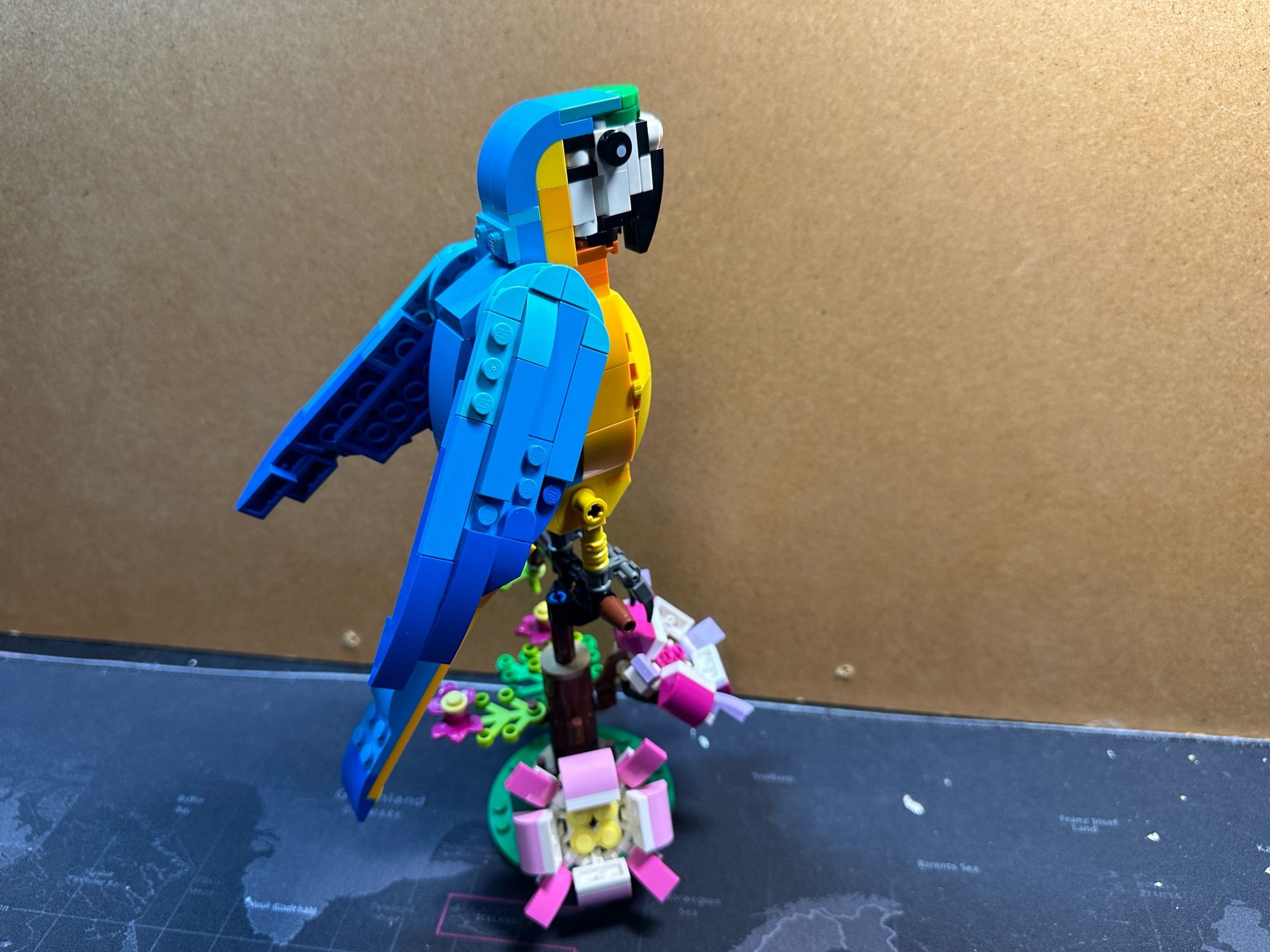 A Lego model of a yellow and blue parrot with flowers under it’s feet.