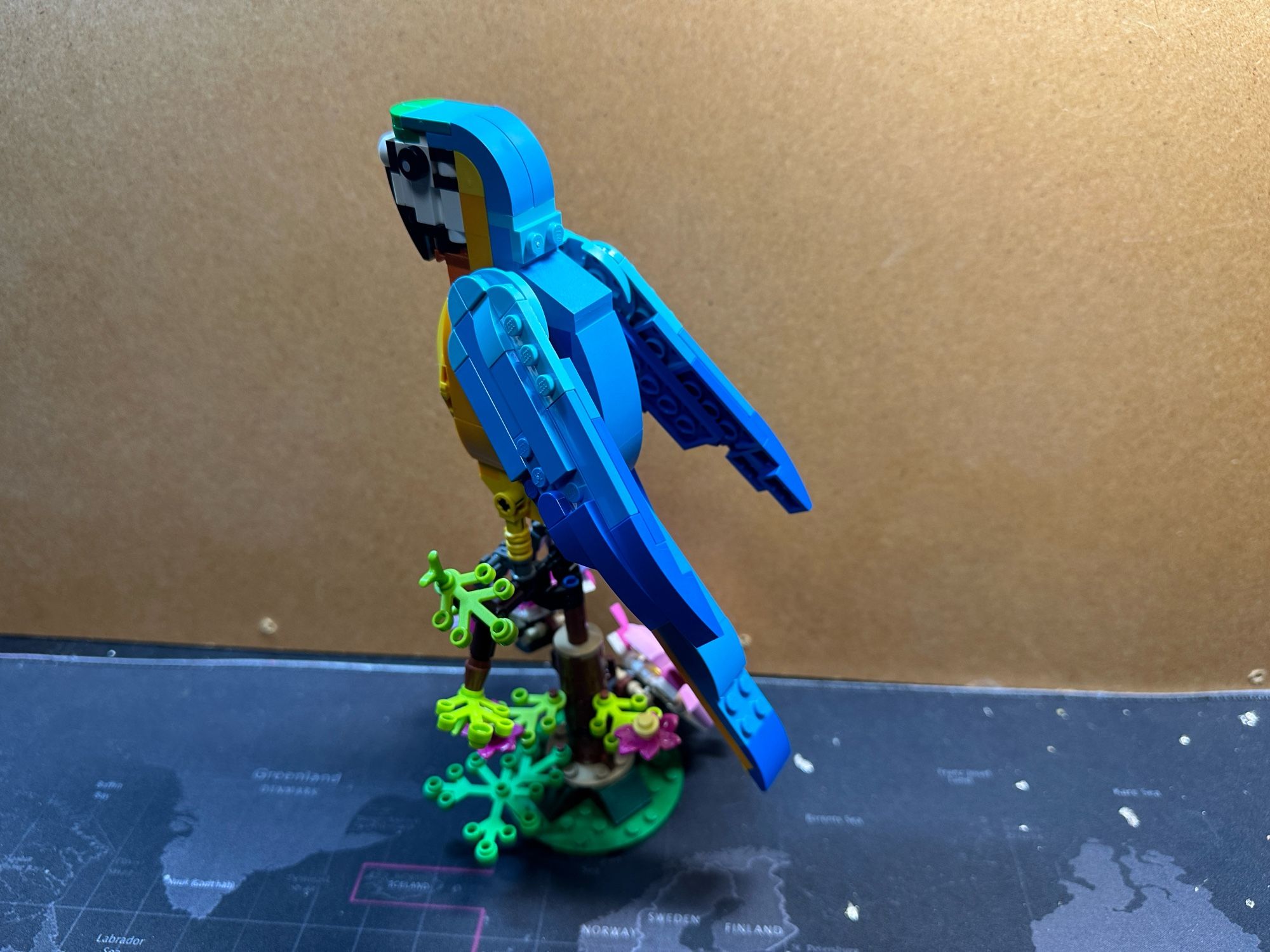 A Lego model of a yellow and blue parrot with flowers under it’s feet.