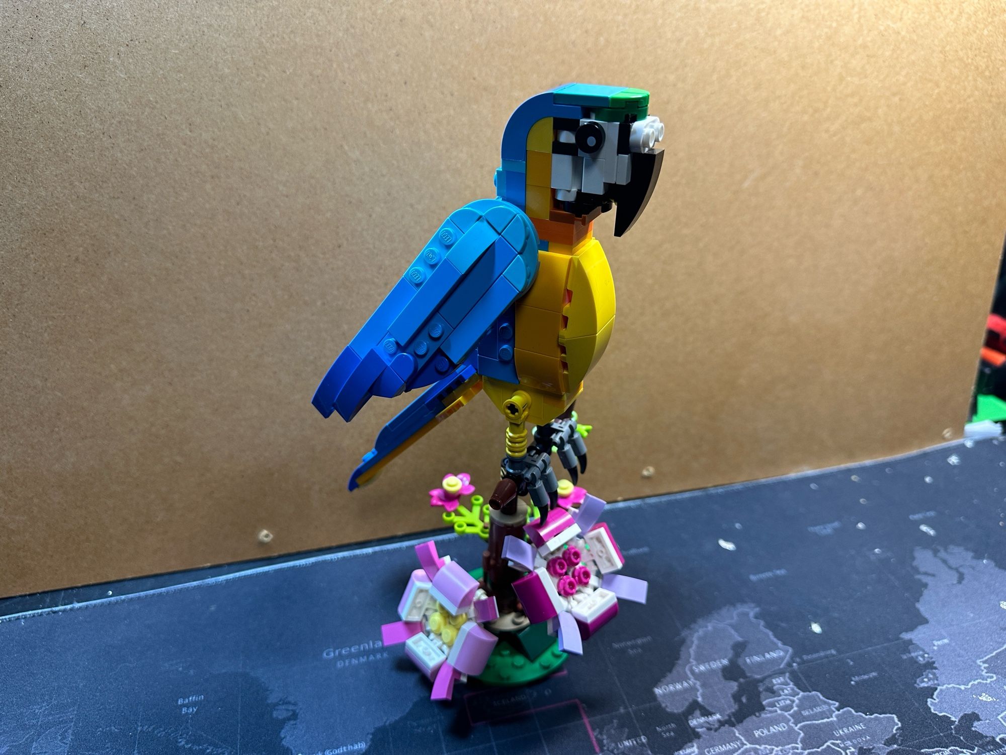 A Lego model of a yellow and blue parrot with flowers under it’s feet.