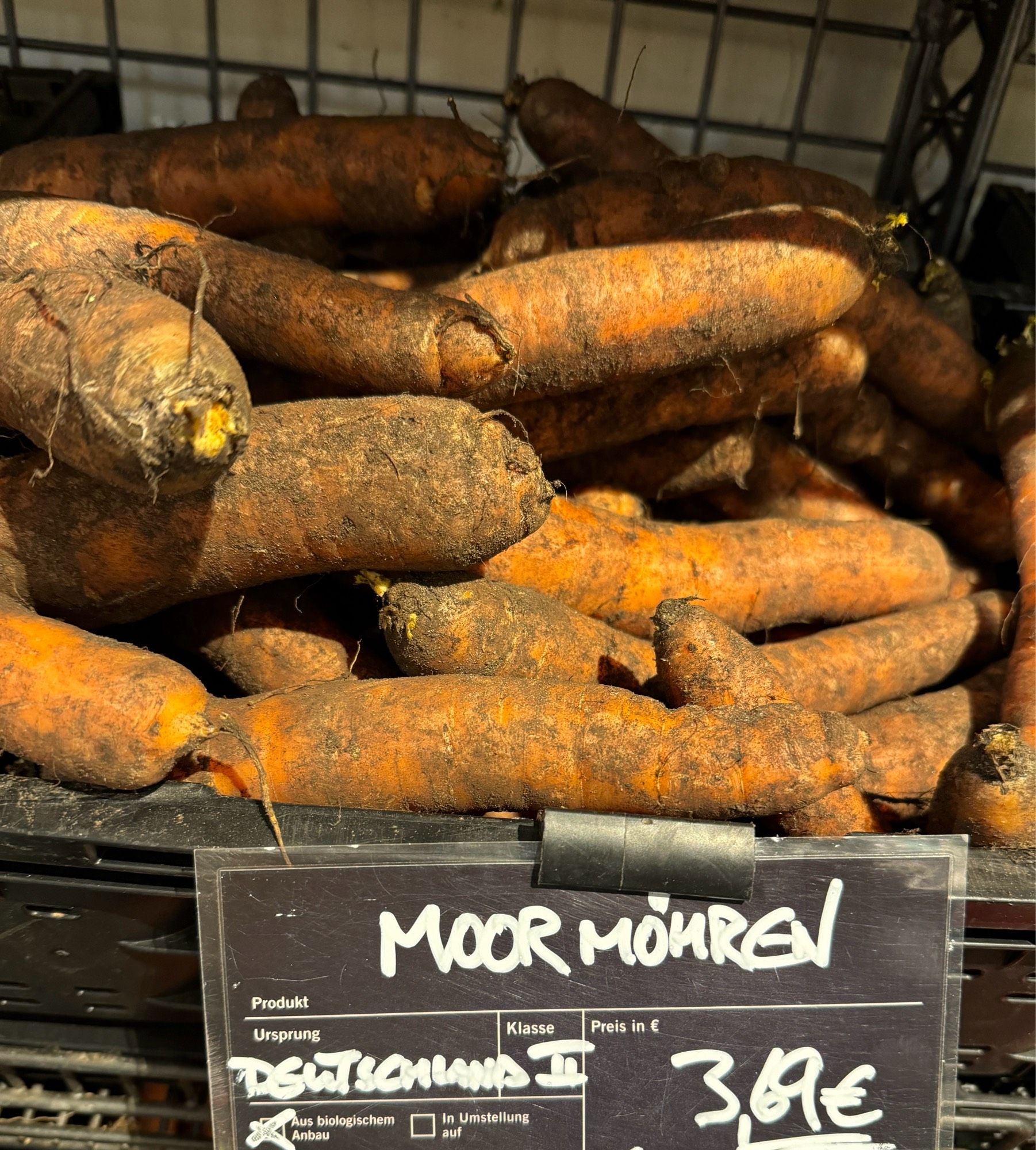 Erdige Möhren in Kiste. Auf dem Preisschild steht: Moormöhren und „aus biologischem Anbau“