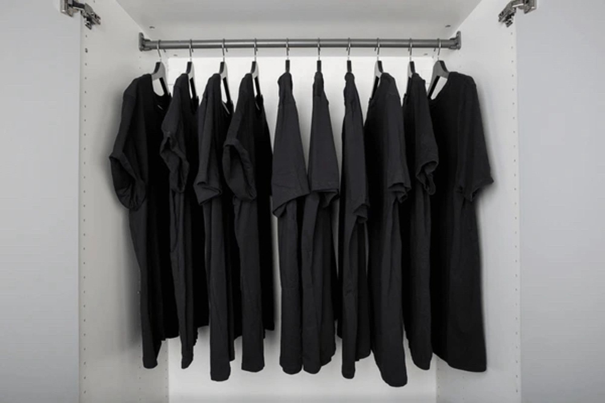 White closet full of black t-shirts hung on hangers.