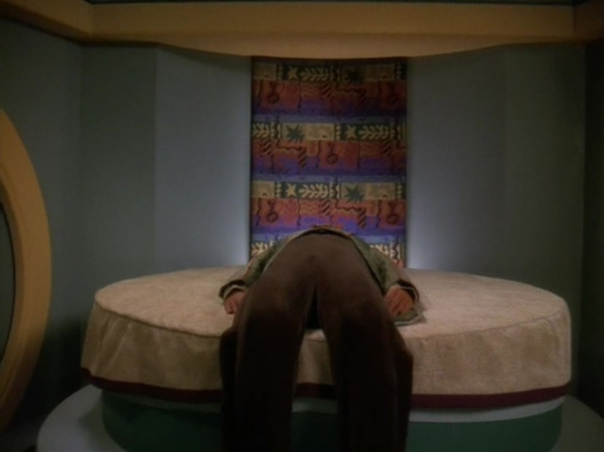 DS9 scene. We're in a home looking at a round bed. We see a person doing that thing where you were sitting on the bed, and then laid down backwards, but kept your feet planted on the ground. No caption.