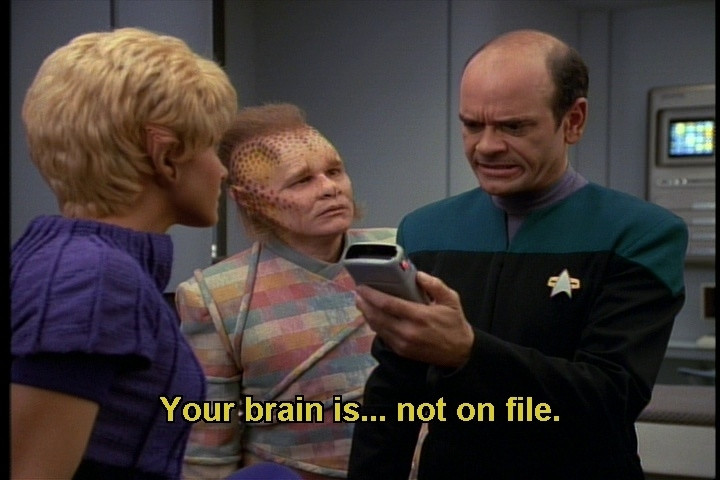 Voyager scene. We're in sick bay with the EMH Doc, Neelix, and Kes. Kes and the Dr look like humans, and Neelix has forehead dots following an aggressively receding hairline and a colorful patterned shirt. The Doctor is looking intensively at his tricorder while Neelix and Kes look at him and wait for some needed info. Closed caption reads, "Your brain is...not on file."