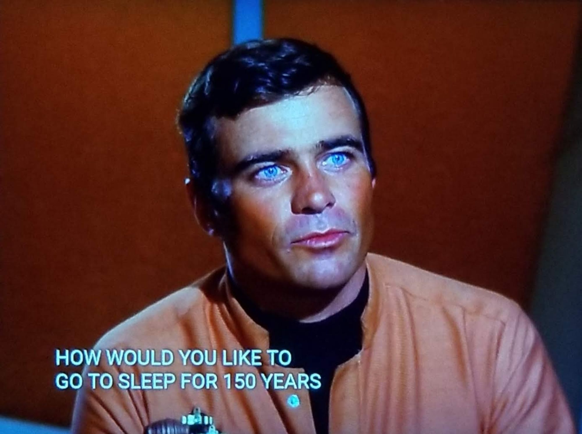 TOS scene. We're in a room.... somewhere. There's a red wall, that's as descriptive as I can get on this one. We're looking at a non regular character, your run of the mill middle aged white fella. He's wearing a salmon looking shirt and looking up with sparkly blue eyes filled with yearning. Closed caption reads, "How would you like to go to sleep for 150 years and wake up in a new world?"