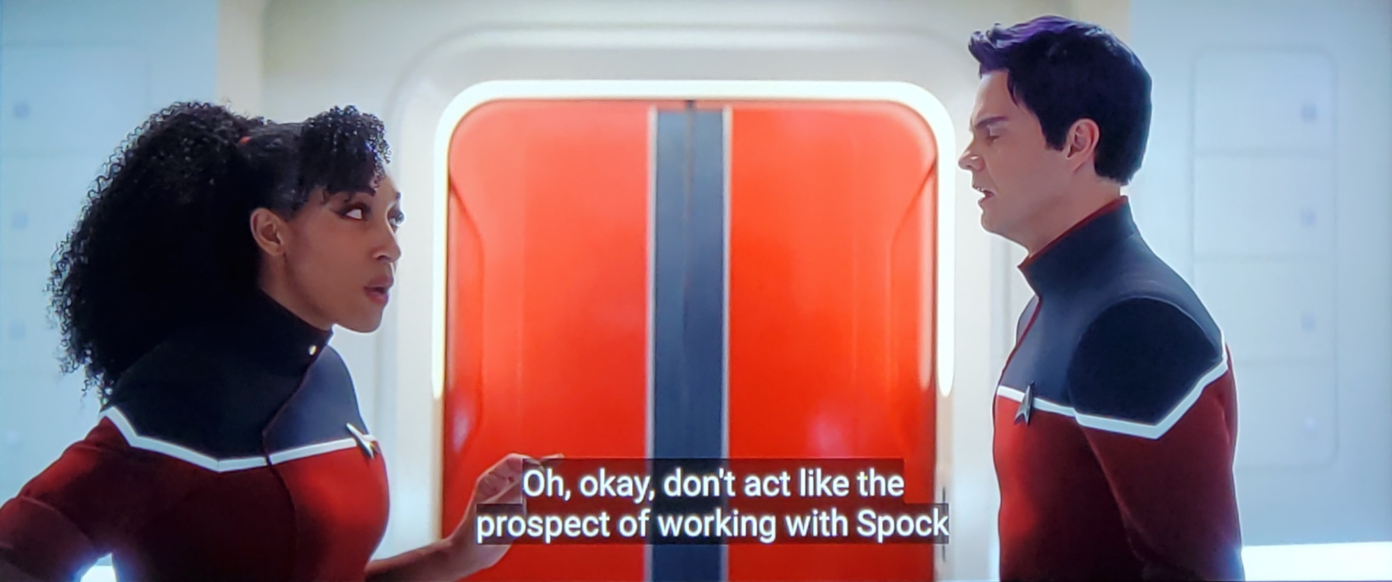 Star Trek Strange New Worlds scene kind of but also Star Trek Lower Decks scene but that's all I can say and if this confuses you just watch more Star trek. Anyhoo, we see a non-cartoon Bradward Boimler and Mariner standing in a corridor on the Strange New Worlds Enterprise outside a beautiful orange door and talking. Both are in Lower Decks era uniforms with red bottom/white crisp stripe across the chestal region and black shoulers. Boims looks distressed, as per usual. He also has slightly purple hair. Mariner is speaking, closed caption reads, "Oh, okay, don't act like the prospect of working with Spock doesn't tick off some weird box for you."