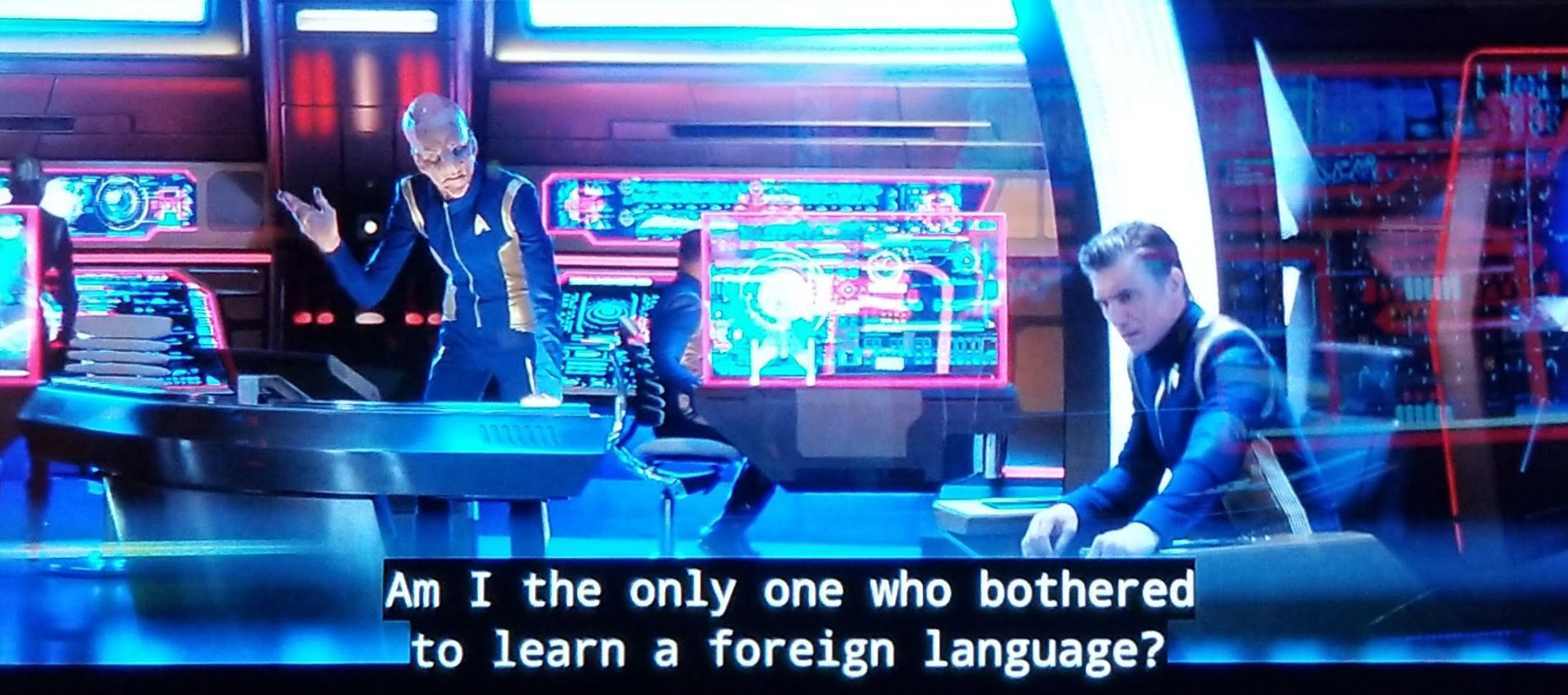 Discovery scene and we're on the bridge. It's filled with lights and bloops and bleeps and screens and neon and consoles and chairs and diagrams and scematics. In focus is Captain beautiful hair Chris Pike sitting in his captain's chair. Near him at a station and standing is the tall and lanky Saru. Both are in uniform, Saru is bald and alien and has hooved feet and some face loaf and we'll just say different looking nostrals. Here, he's leaning over his console and raising a hand in exasperation. Closed caption reads, "Am I the only one who bothered to learn a foreign language?"