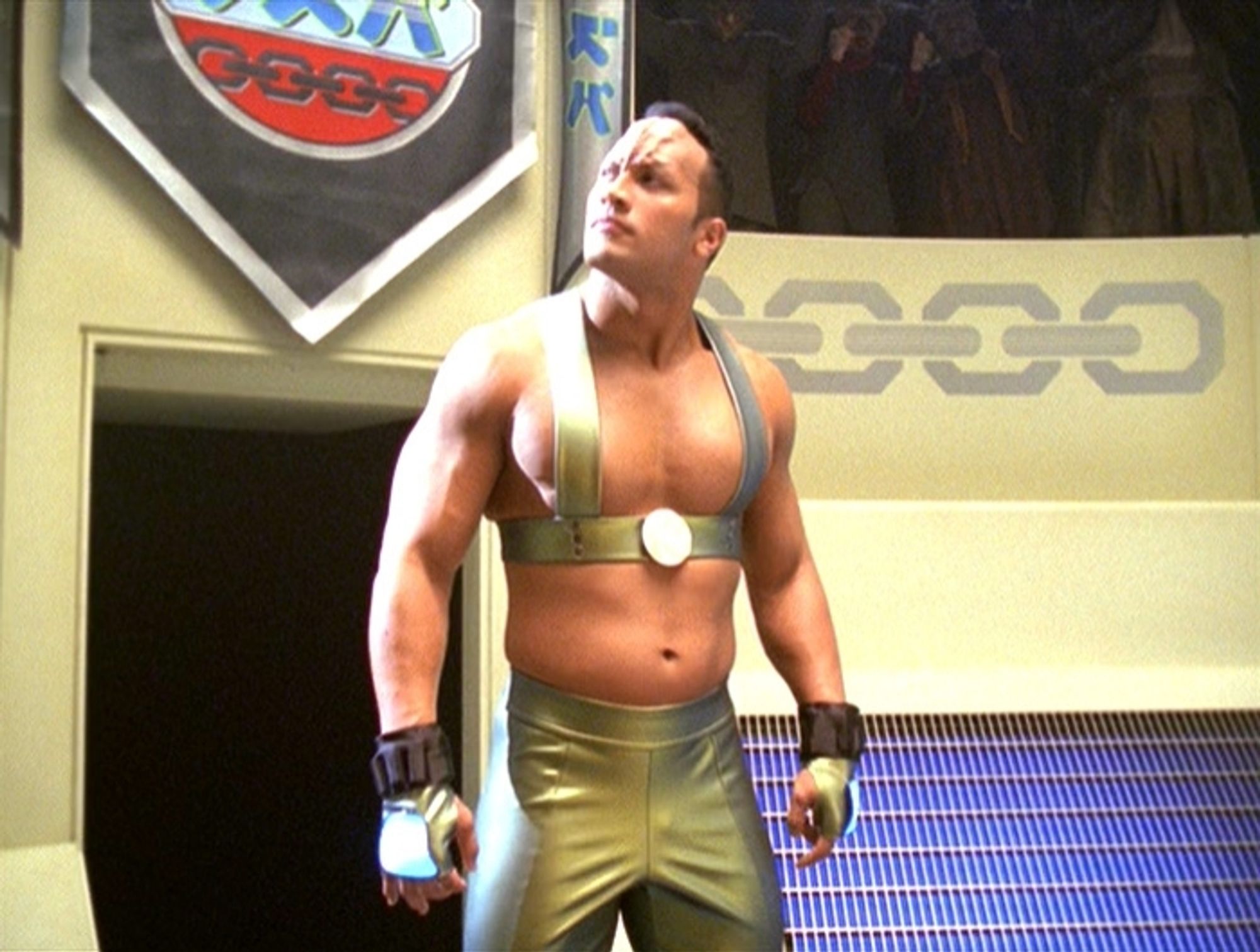 Voyager scene.  We're in what looks like an arena of some kind and the Rock, from TV's "wrestling" and "Jumanji" and "Ballerz" has just emerged from an entrance. He's wearing gold leather pants and a golden upper body strap type thing. It's like what the back of a bra looks like, but on the front, and does cover the nips, in case you were wondering. He's got some wrist and glove accoutrements happening and generally looks like he's about to be involved in some kind of sporting contest. He also has some forehead loaf to indicate he's an alien and not just, "The Rock" in space.  There are some stadium onlookers in the background and some symbols that appear on the arena wall behind him. Back to The Rock, he's posing and looking all swol and looking up and seems like he's sniffing something while admiring how much people love him. No caption.