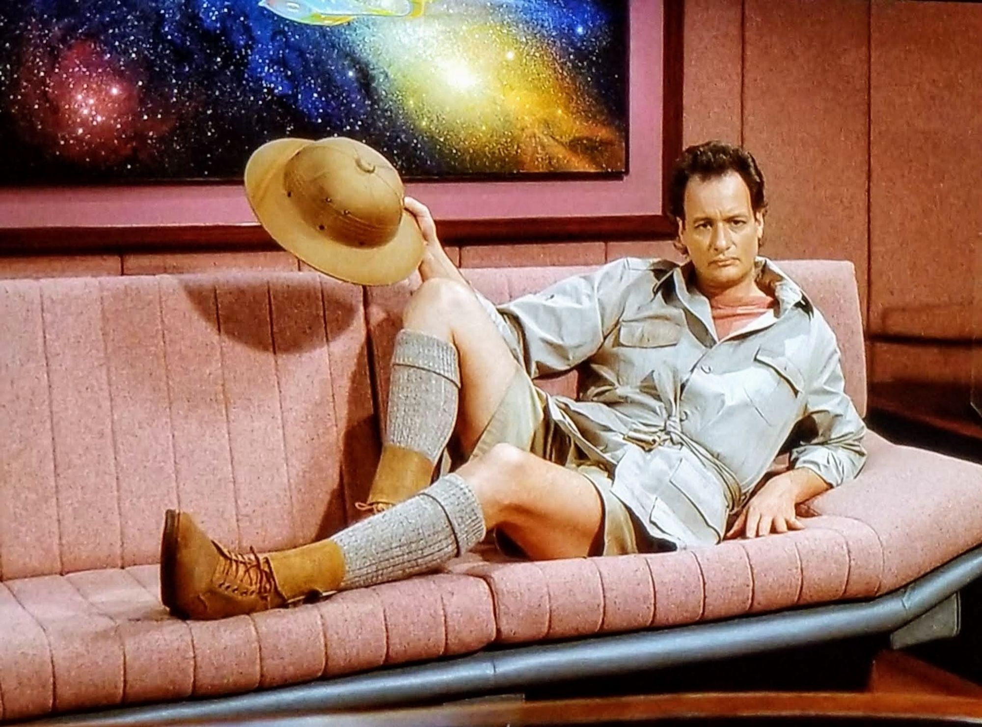 TNG scene. We're in captain Picard's ready room, looking at his couch, which sits under a painting of the Enterprise in a nebular in space. On the couch, half laying down half sitting all "lookie here" seductive like is Q, dressed in a all tan safari outfit. It's like the pose someone would do if they were in a bikini while sitting on a convertible. No caption.