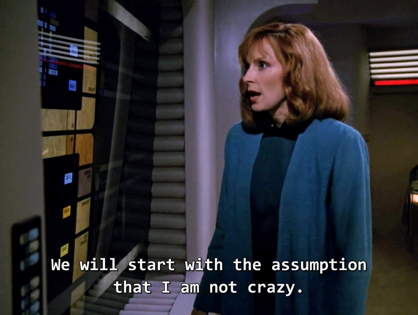 TNG scene. Dr Beverly Crusher stands at a wall computer console unit on the Enterprise. She's wearing a blue doctor coat. That's about it, nothing too wild in this one. Closed caption reads, "We will start with the assumption that I am not crazy."