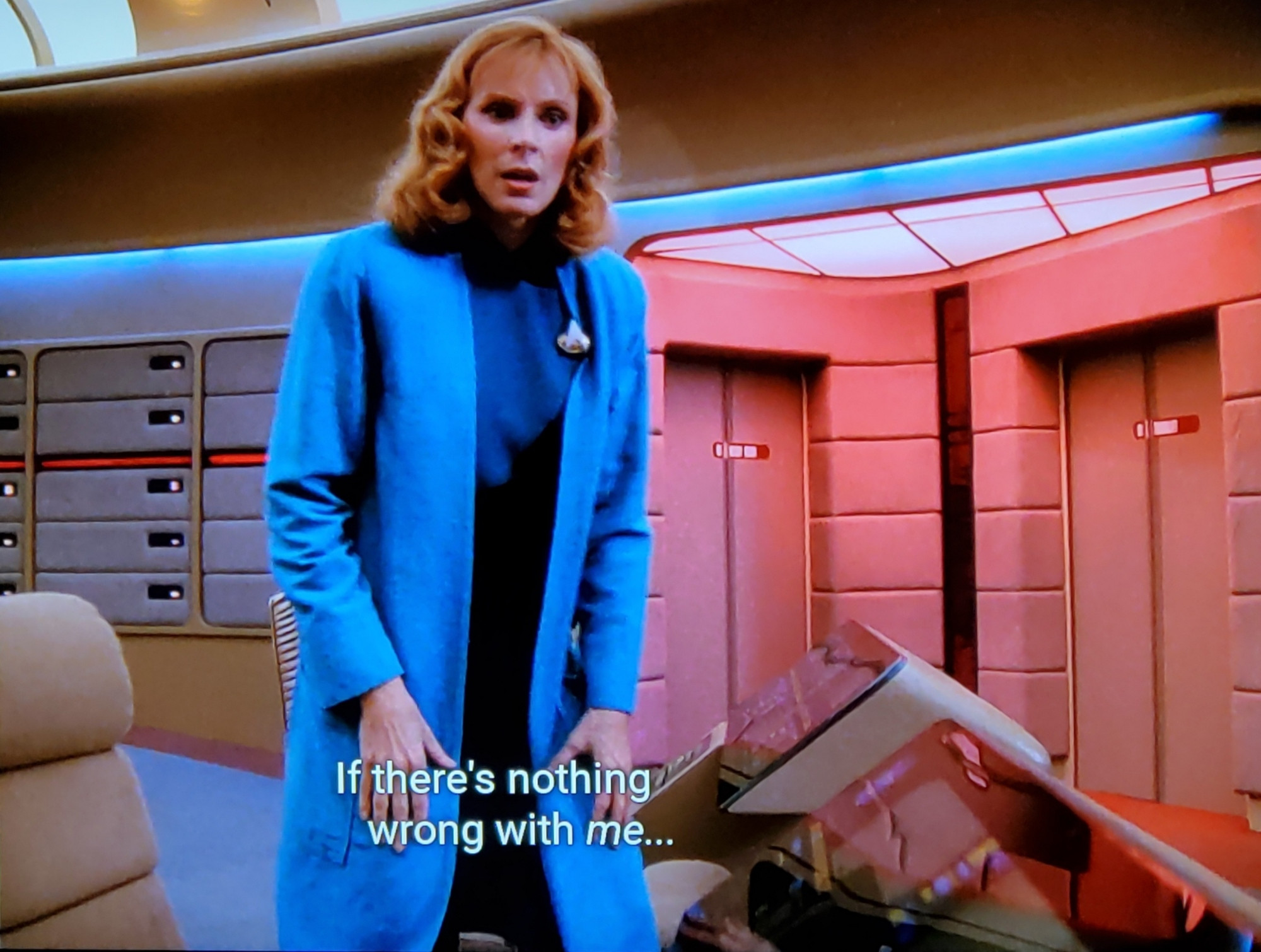 Star Trek The Next Generation scene and we're on 'da bridge, down near the laid back chairs where one would navigate the ship. But the bridge is EMPTY OF OTHERS except for Dr Crusher. Where is everyone? We'll never know. Back to Bev, she's standing in the first picture and then in the second frame sits in the chair looking puzzled and stressed, while red alert lights shine all around.  Closed caption reads, "If there's nothing wrong with me... maybe there's something wrong with the universe."