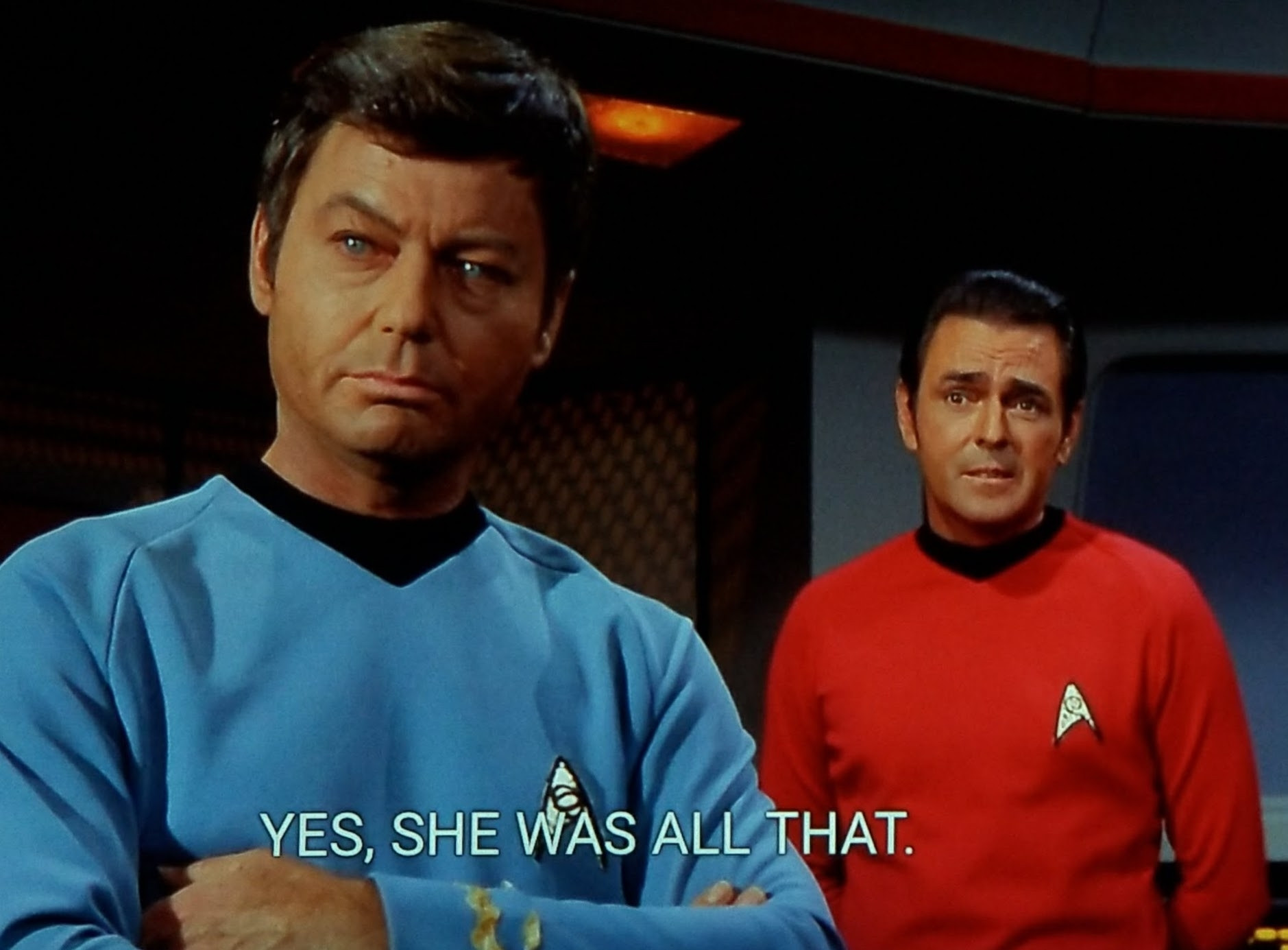 Star Trek The Original Series scene. Dr. "Bones" McCoy stands in blue uniform, arms crossed, looking lost in a thought. Scotty in bright red uniform stands behind him a few steps looking like he's just about to say 'aye, lass' or some such Scottish phrasing. Closed caption reads, "Yes, she was all that."