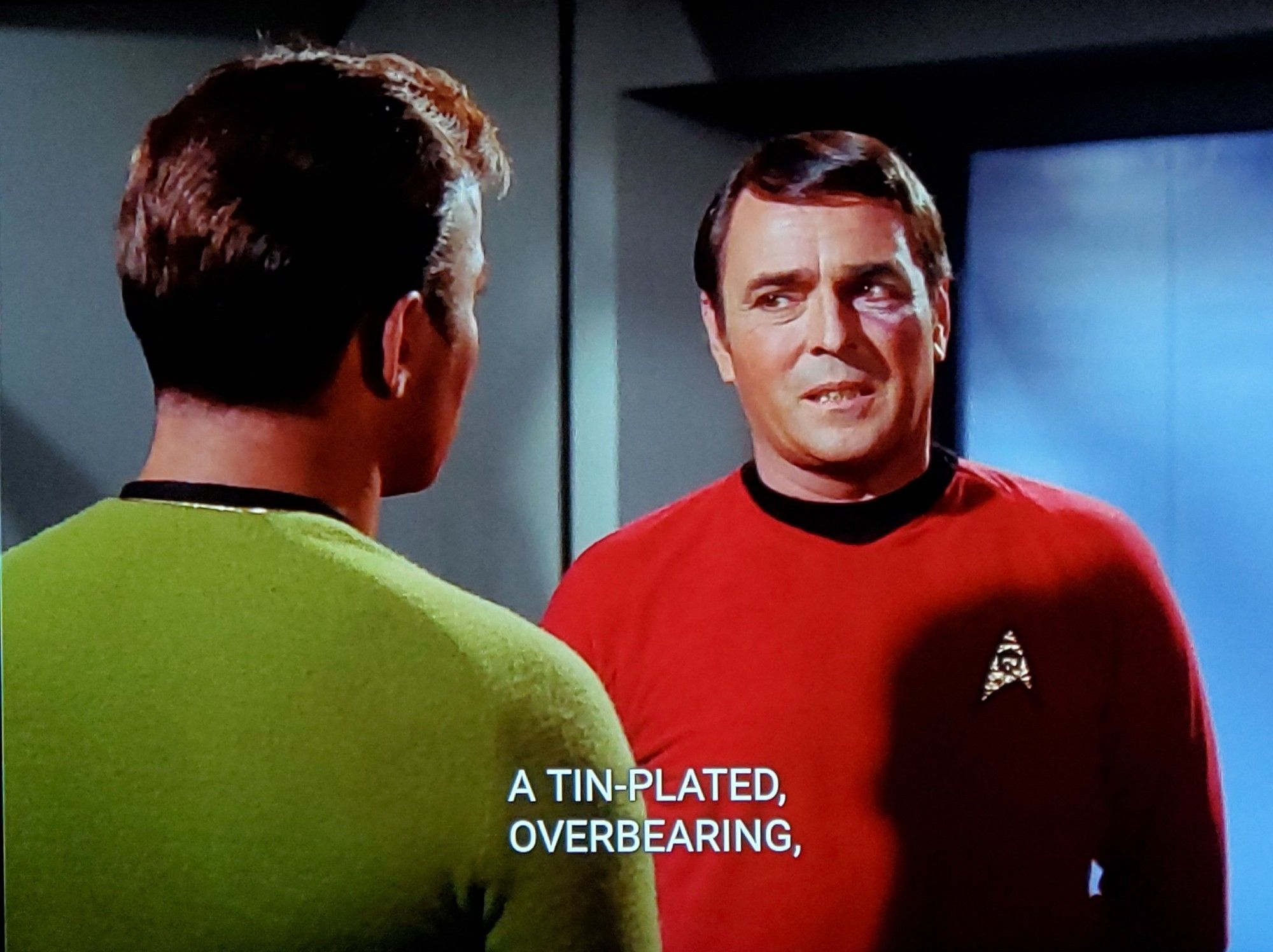 TOS scene. Scotty and Kirky are talking. Scotty in red uniform, Kirk in Green but also maybe yellow my camera sometimes changes hues and whatnot. We're looking over Kirk's shoulder at Scotty in the first pic and reversed that on the second and Scotty looks like he's giving Kirk bad news. Closed caption reads, "A tin-plated, overbearing, swaggering dictator with delusions of godhood."